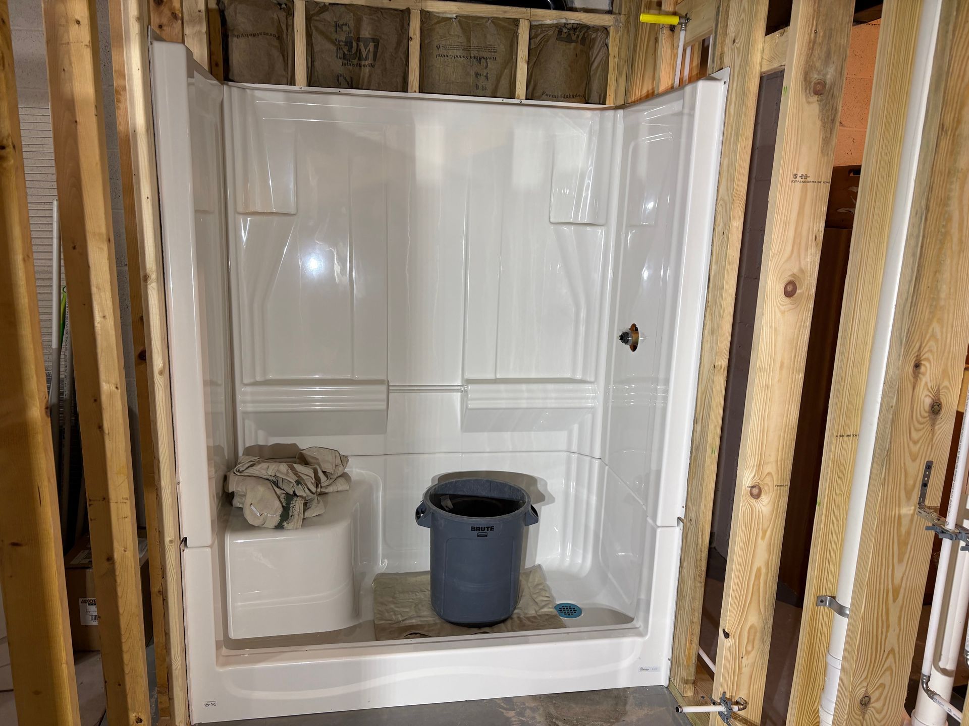 White shower stall installed in a framed-in bathroom, with a trash can and towels inside.