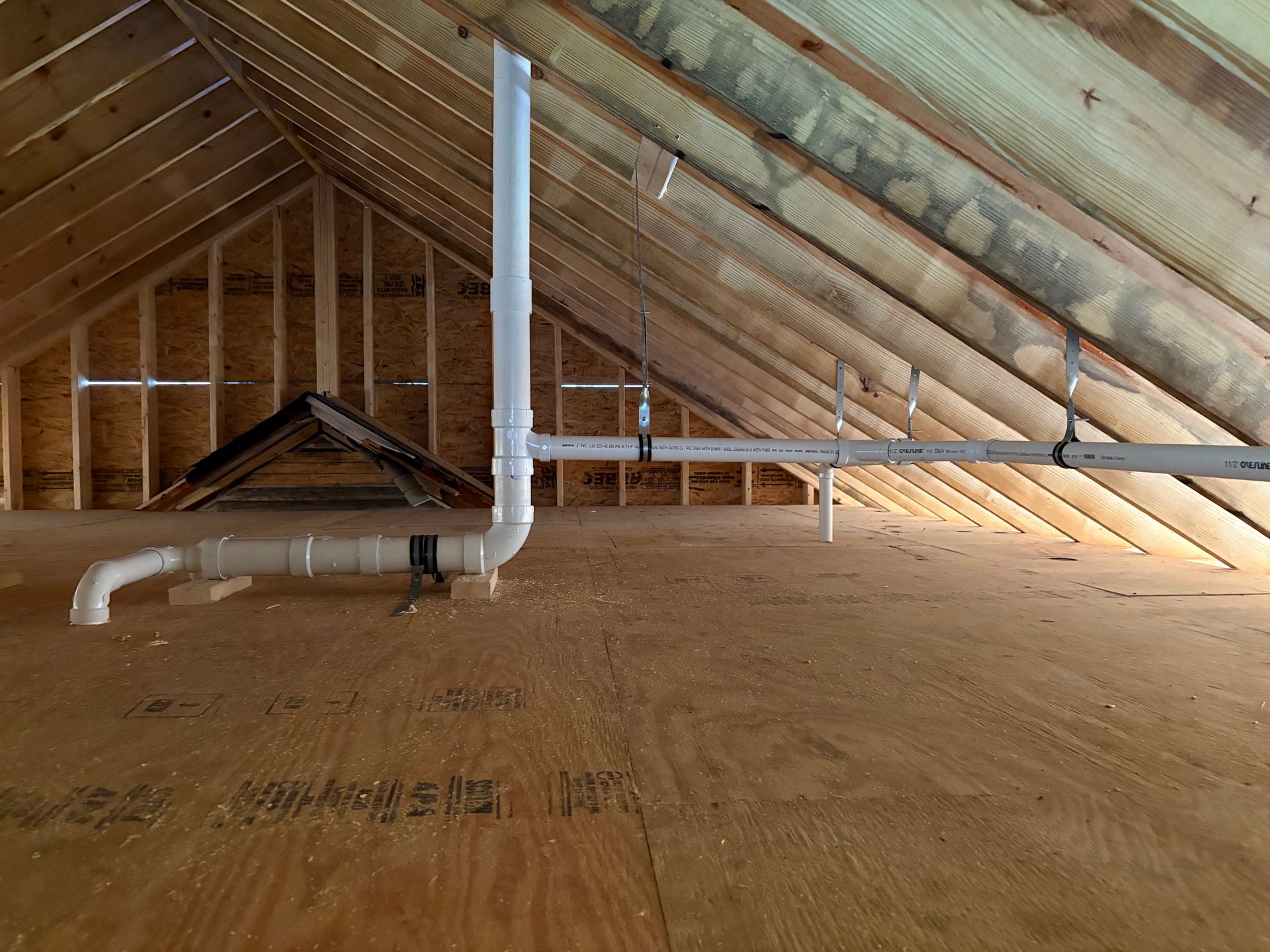 Attic interior with exposed wooden beams, insulation, and PVC pipes extending upwards.
