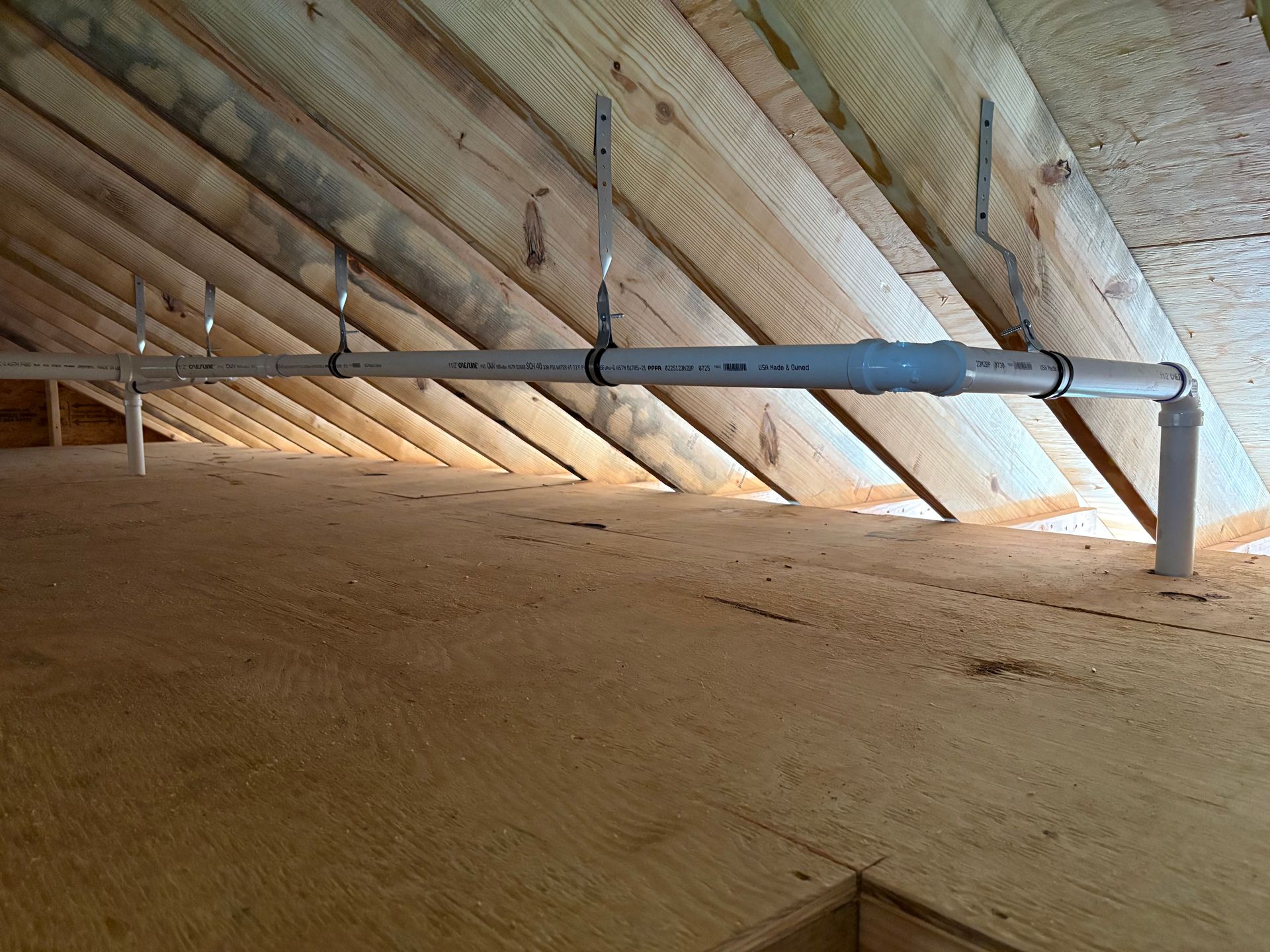 PVC pipes suspended from rafters in an attic space.