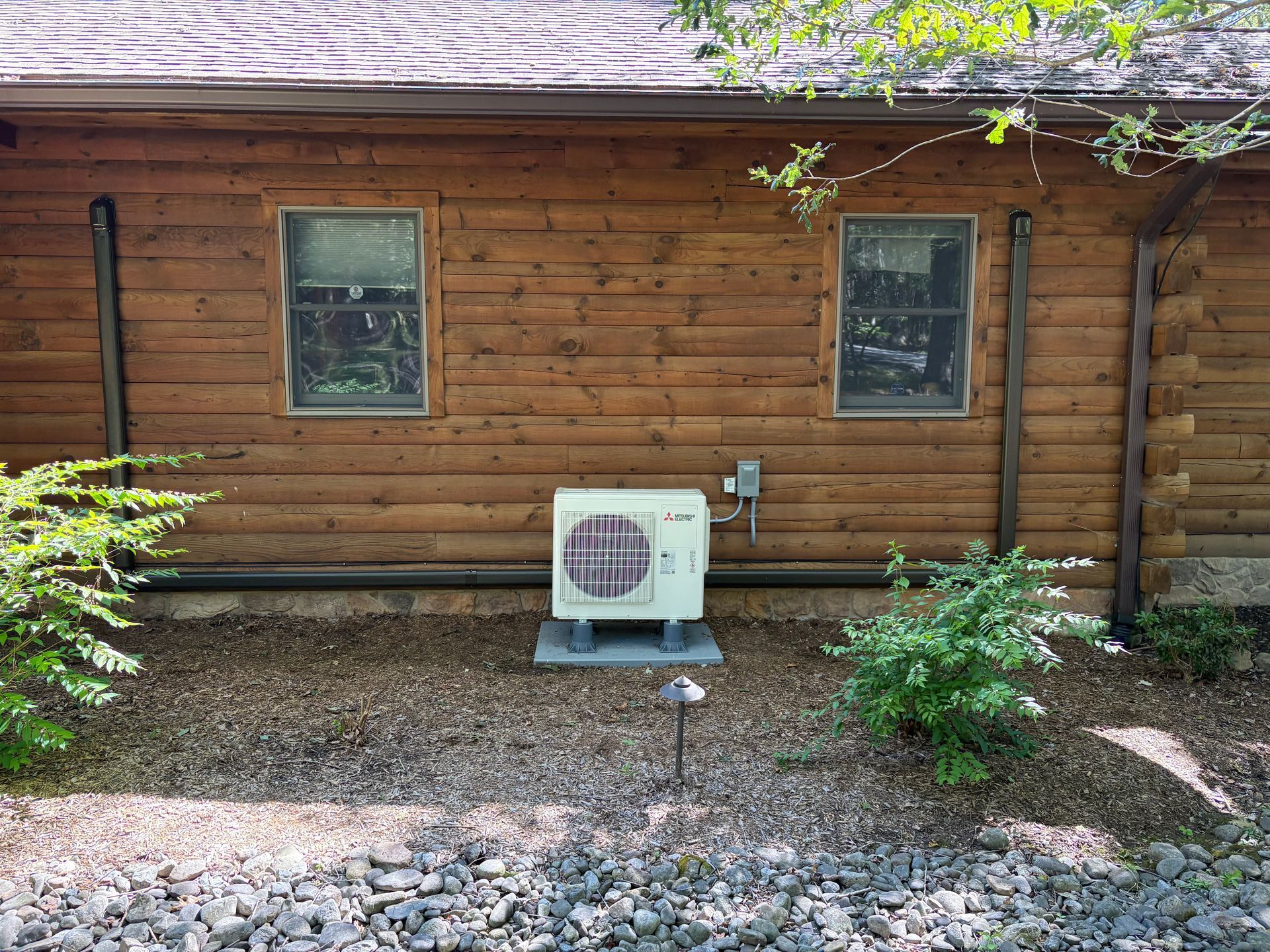 Air conditioning unit outside a log cabin, near two windows.
