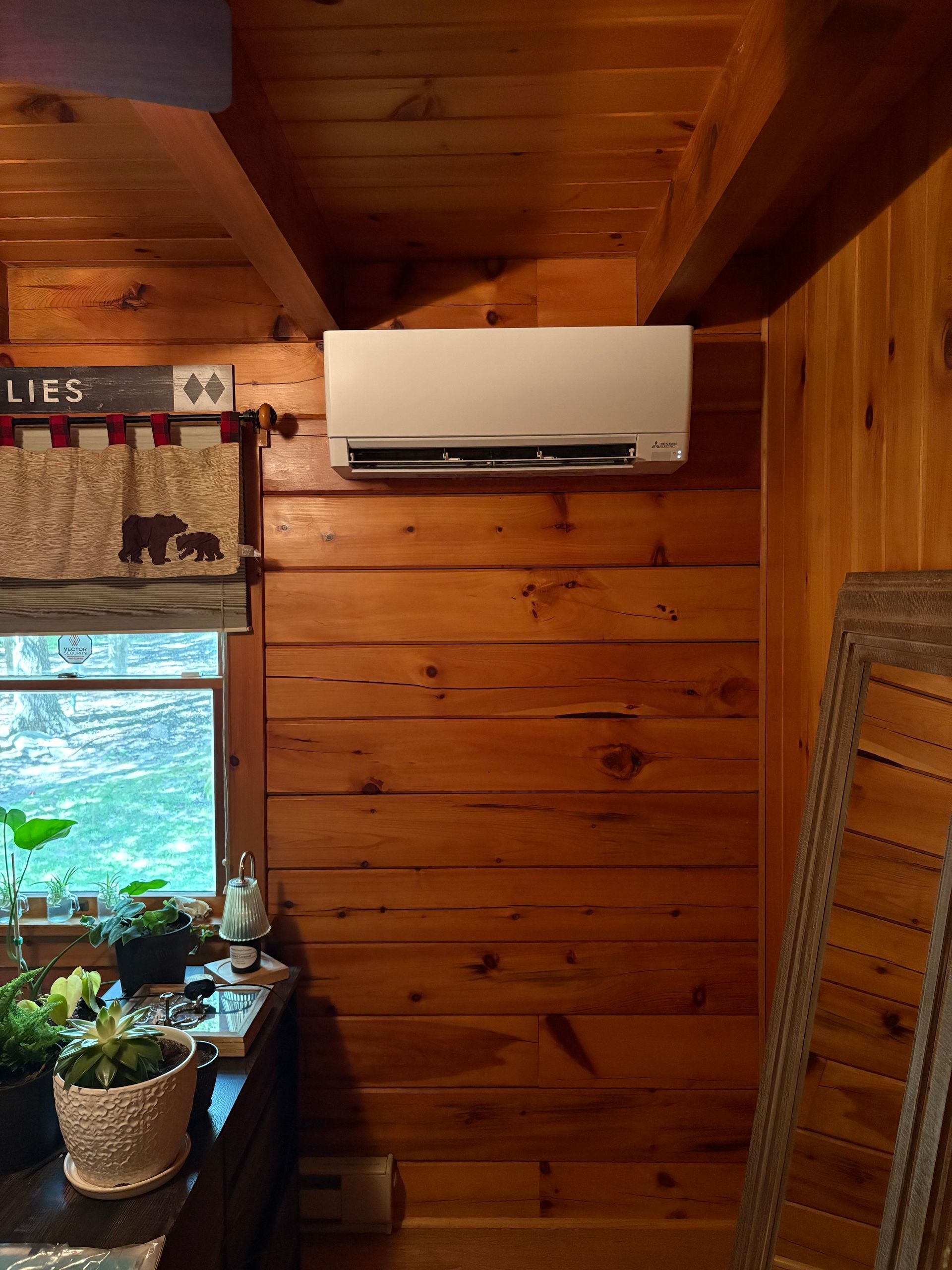 Air conditioning unit mounted on a wooden wall in a rustic cabin.