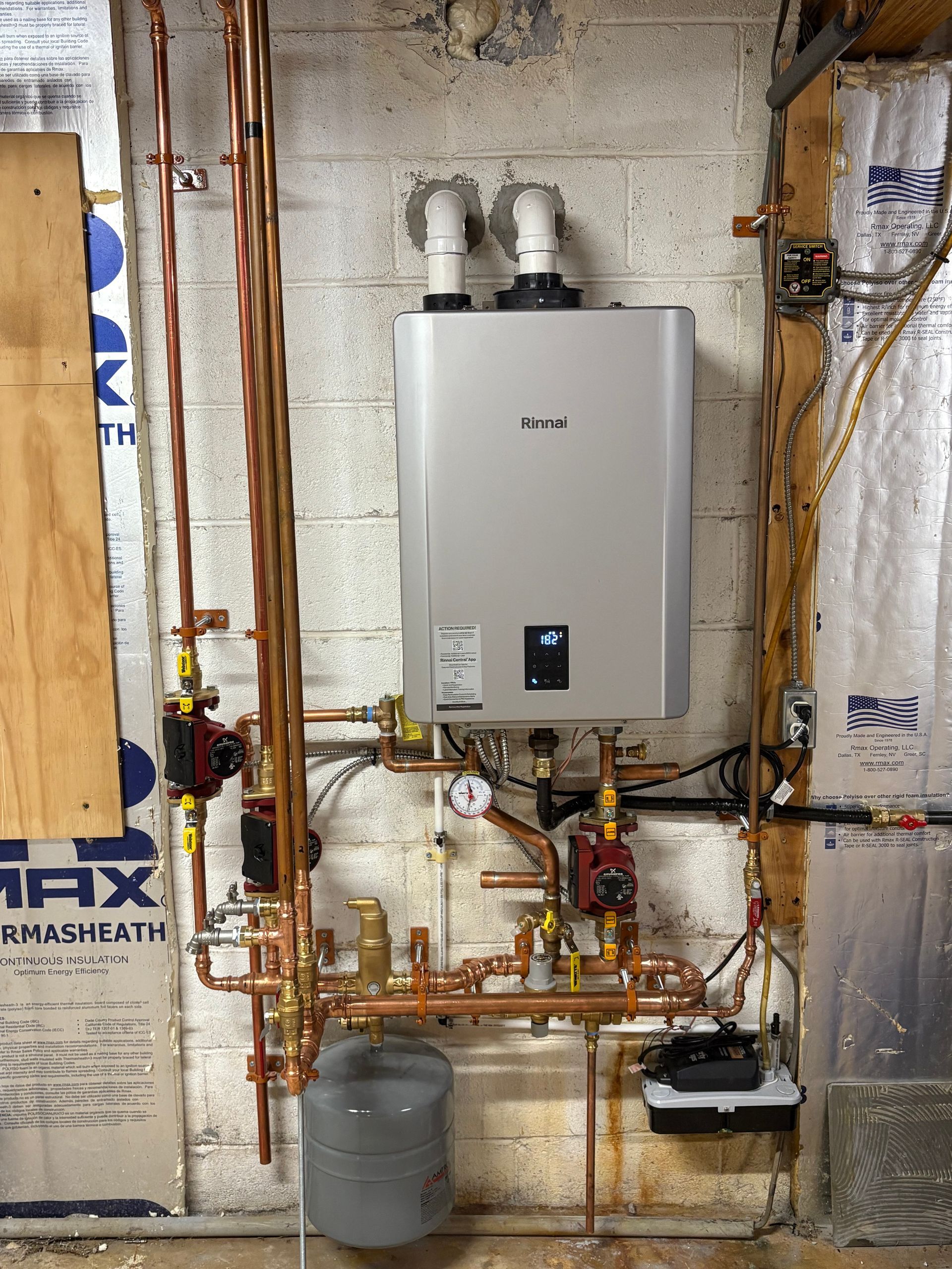 Tankless water heater with copper pipes on a basement wall.