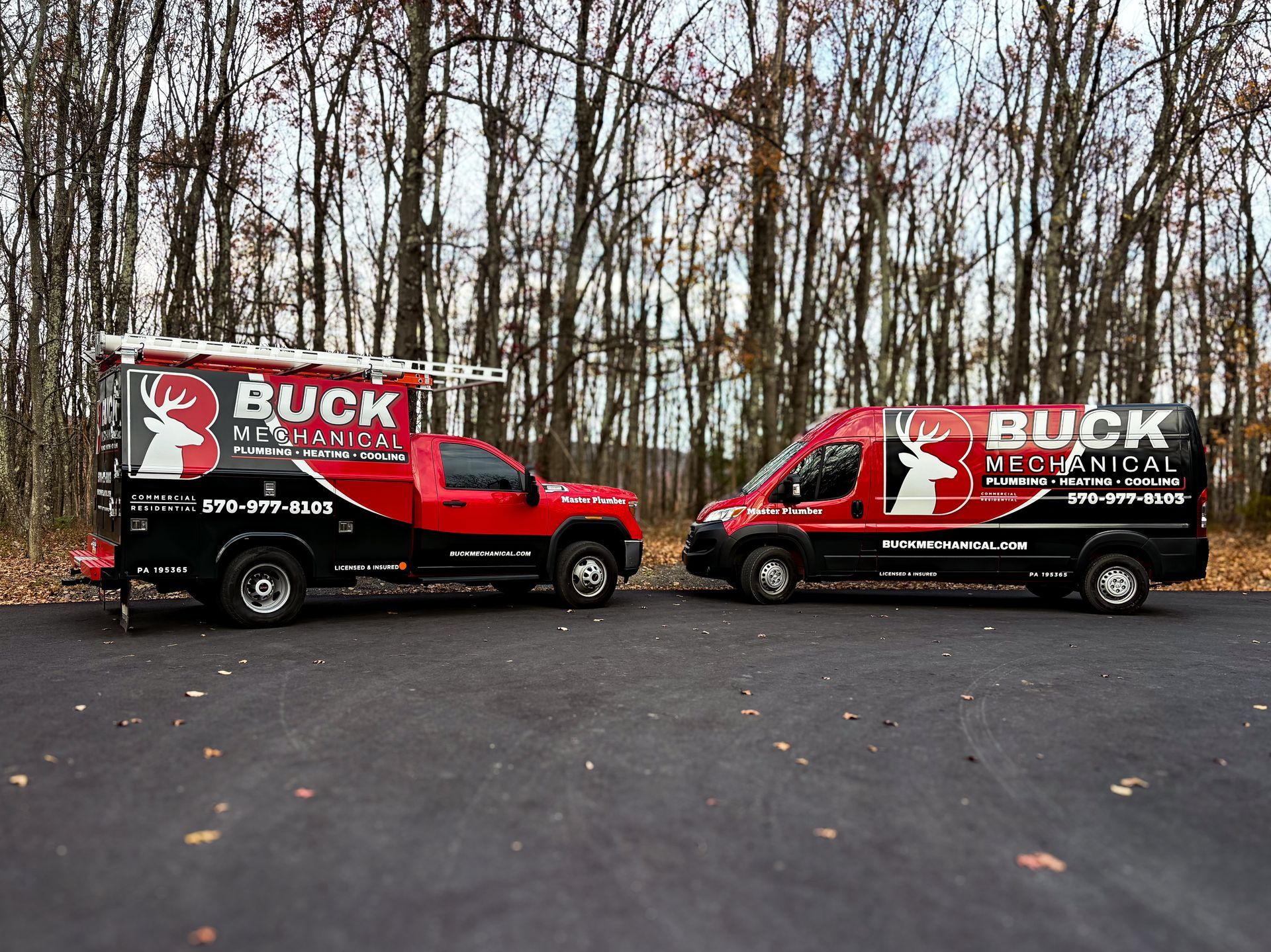 Red and black Buck Mechanical service trucks parked on a road in front of trees.