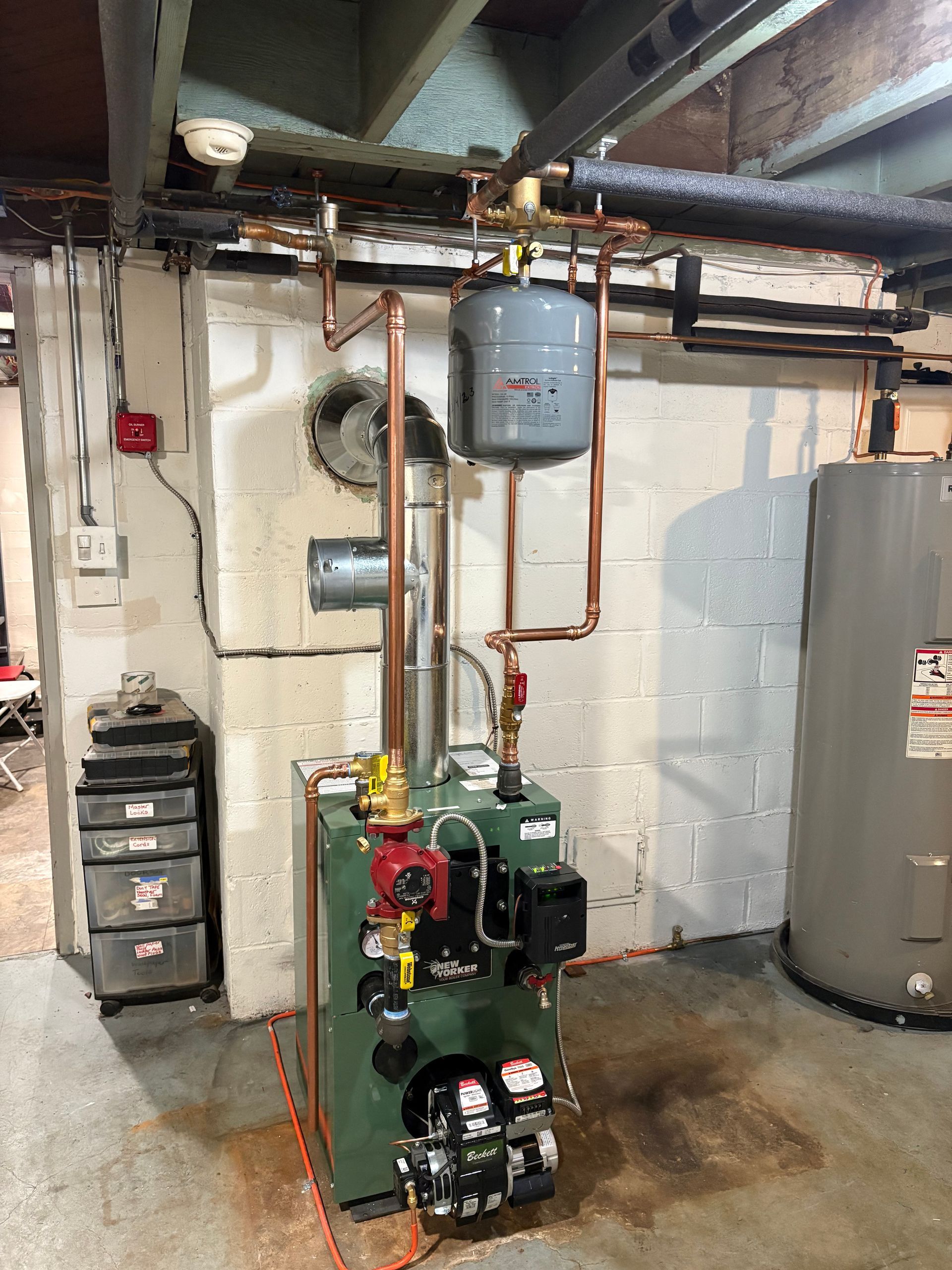 Green boiler with copper pipes, expansion tank, and water heater in a basement.