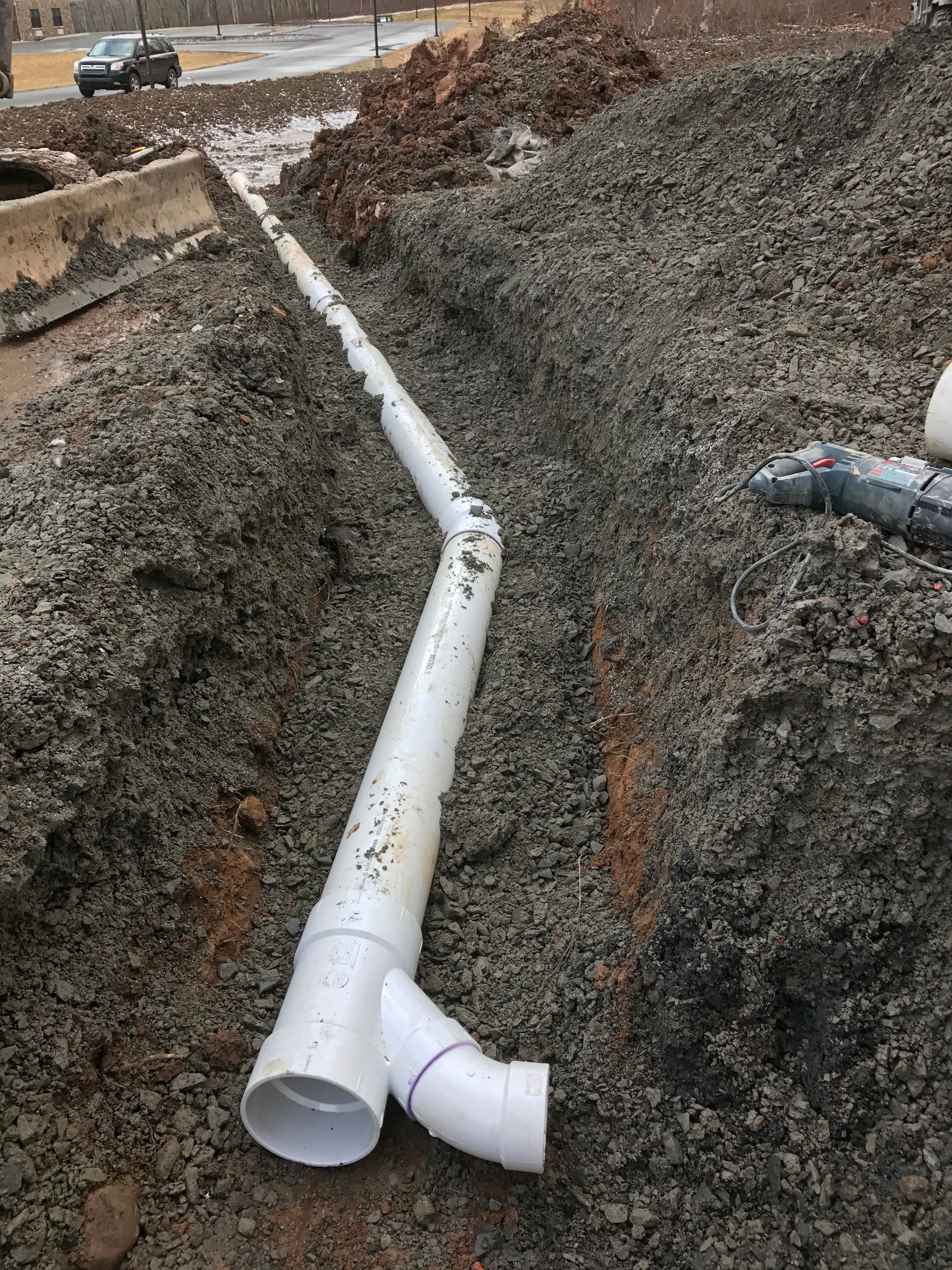 White PVC pipes in a trench with gravel, likely for drainage during construction.