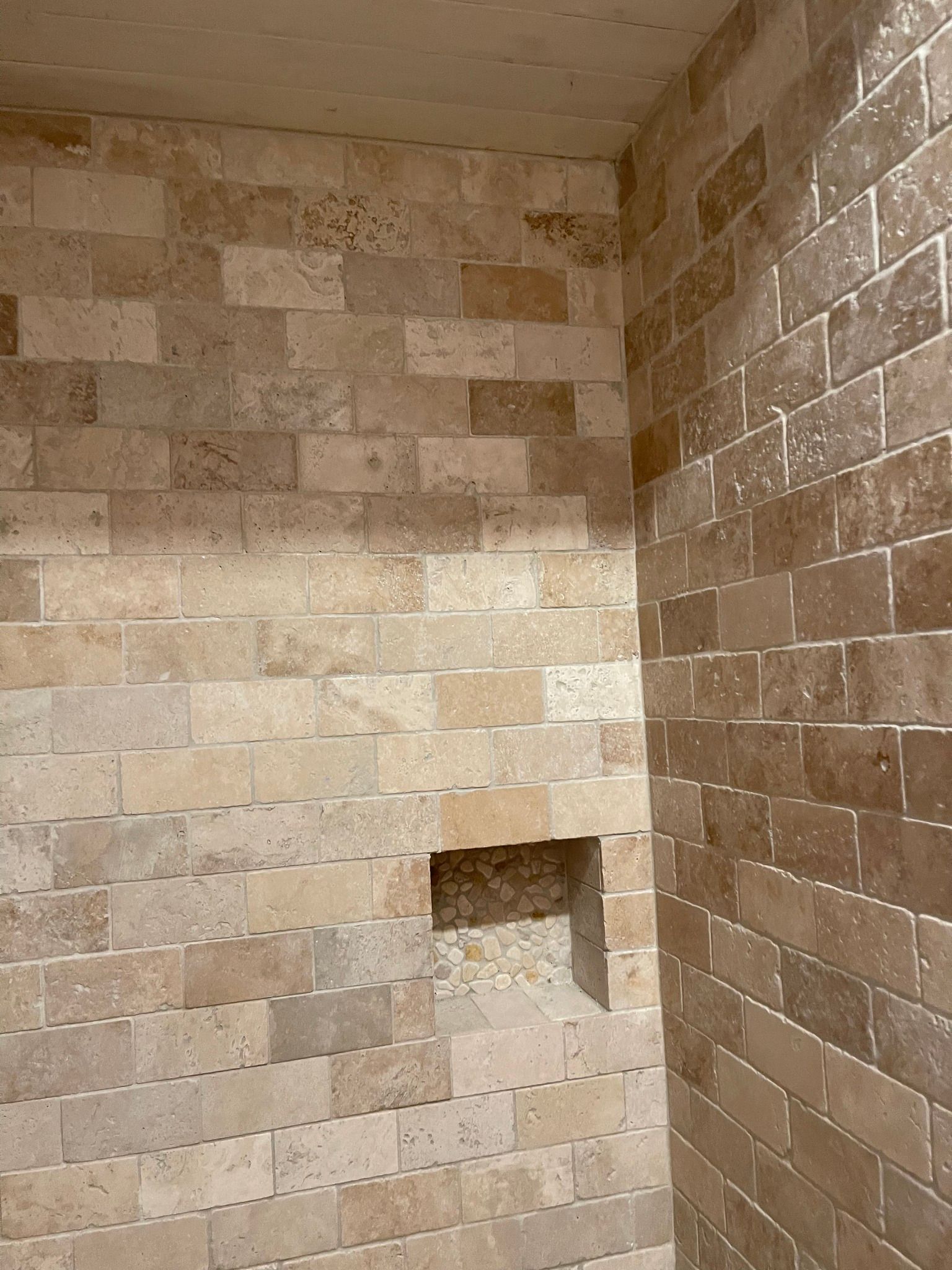Shower with beige brick-patterned tile walls, featuring a recessed shelf.