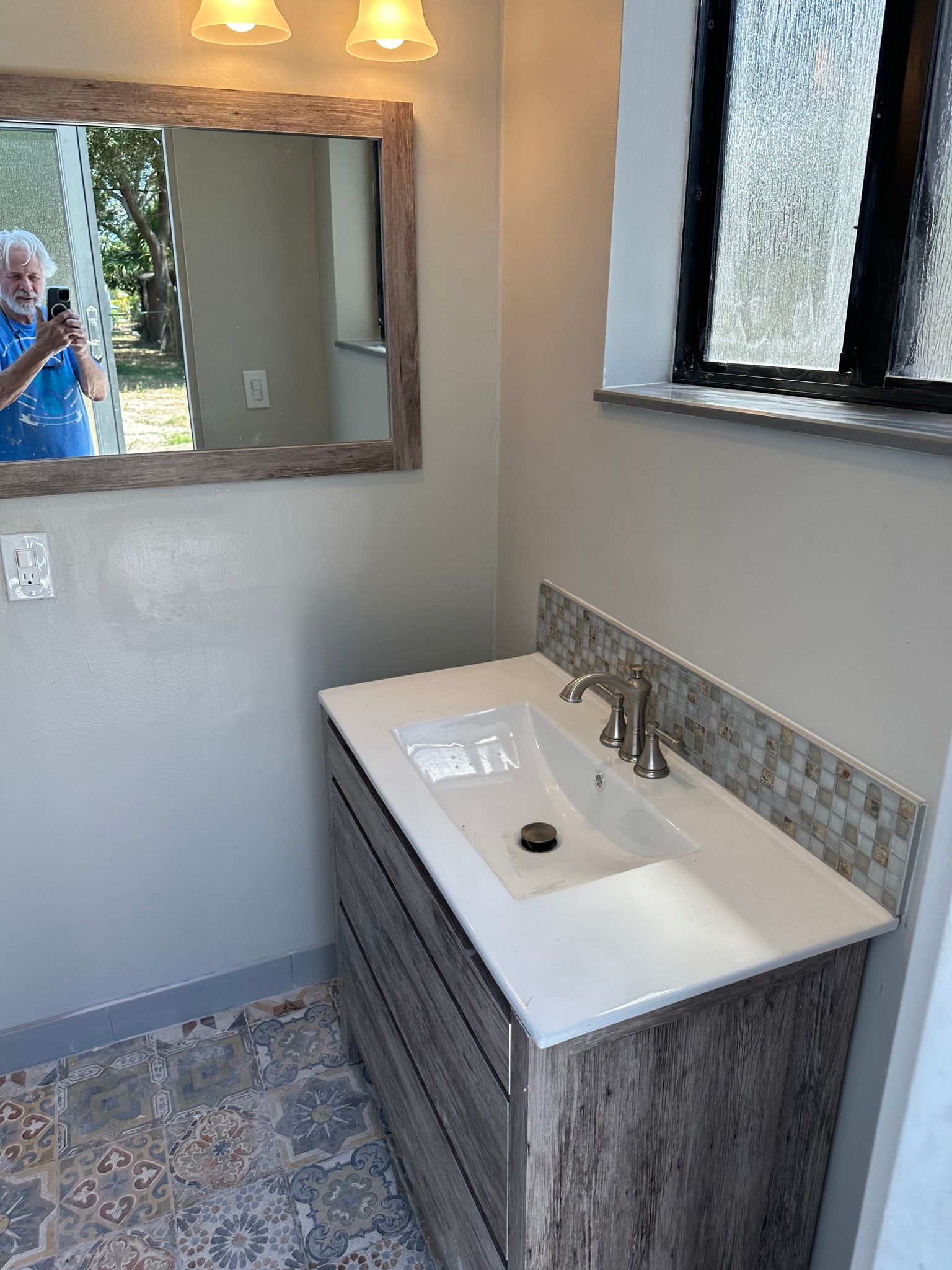 Bathroom with vanity, mirror, and sink; light gray walls, and patterned floor tile.