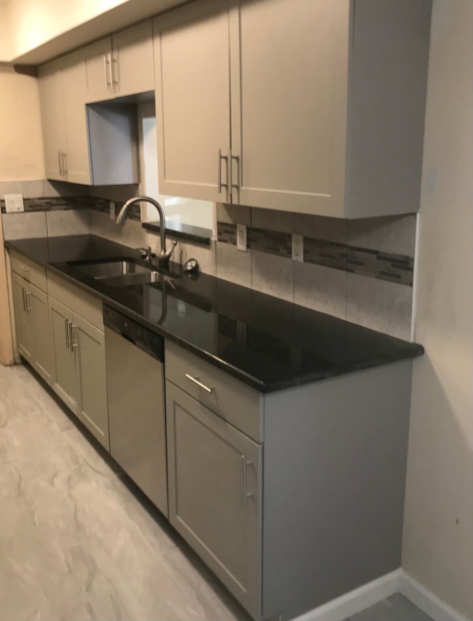 Gray kitchen cabinets with black countertop, stainless steel appliances, and a decorative backsplash.