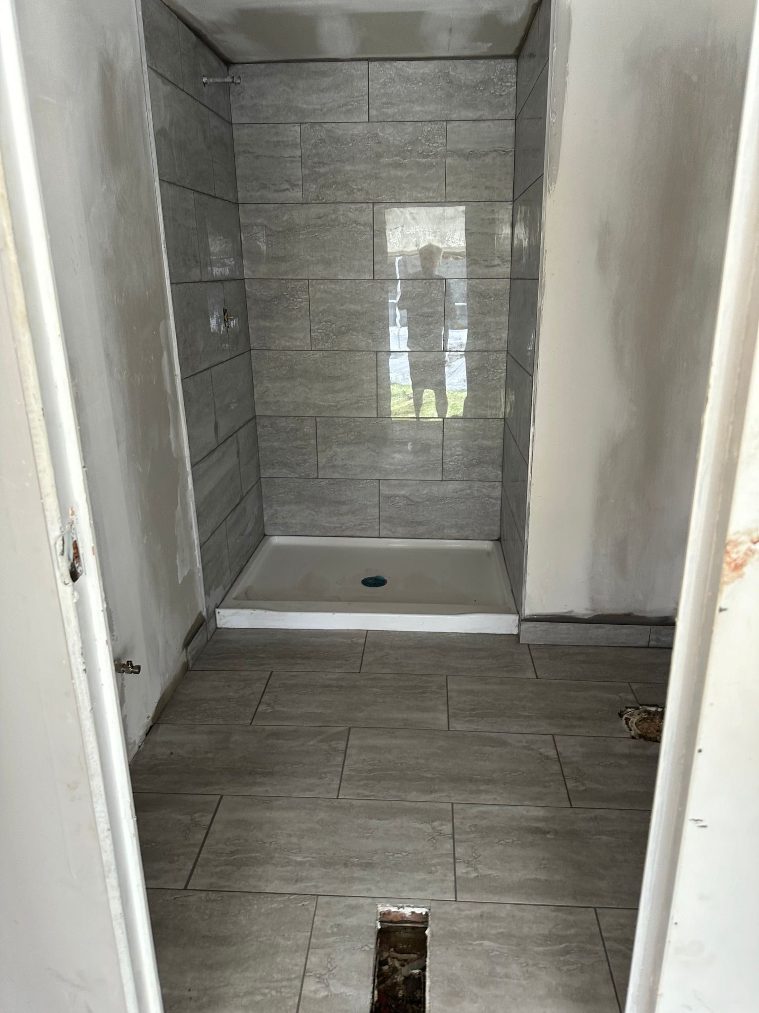 Shower stall under construction with gray tile walls and floor.