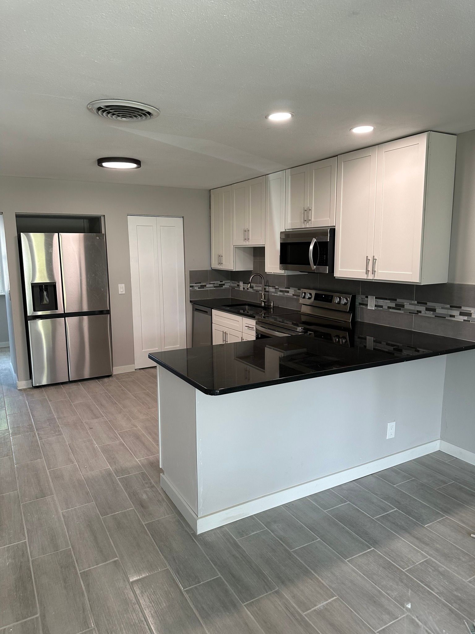 Modern kitchen with stainless steel appliances, gray cabinetry, and black countertops.