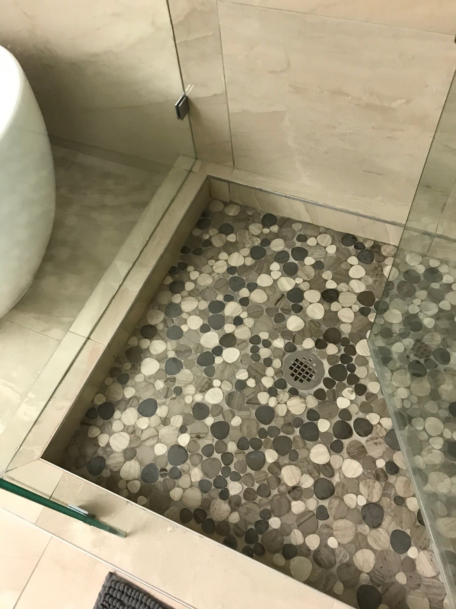 Shower with pebble tile floor, glass door, and tan walls.