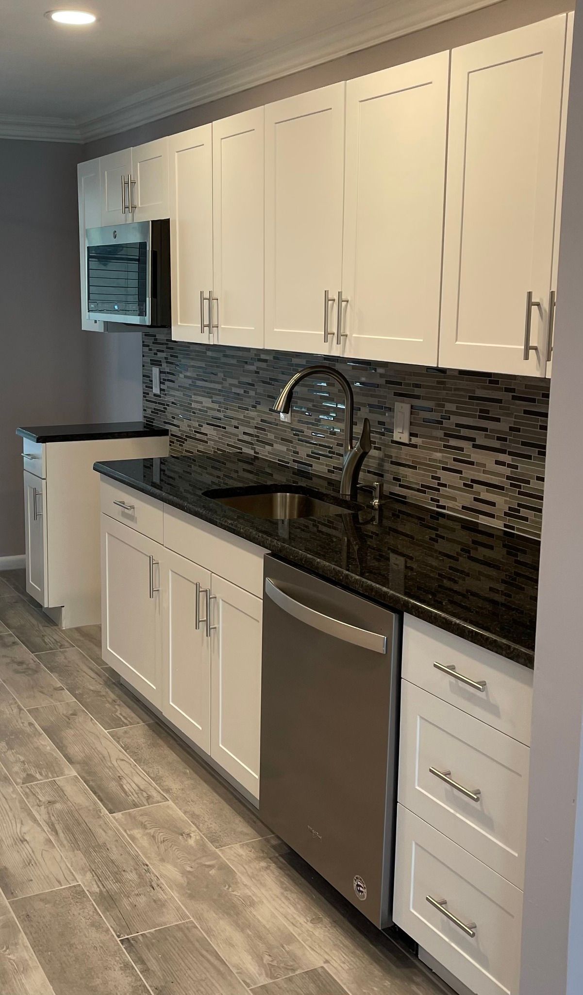 White kitchen with black countertop, stainless steel appliances, and grey backsplash.
