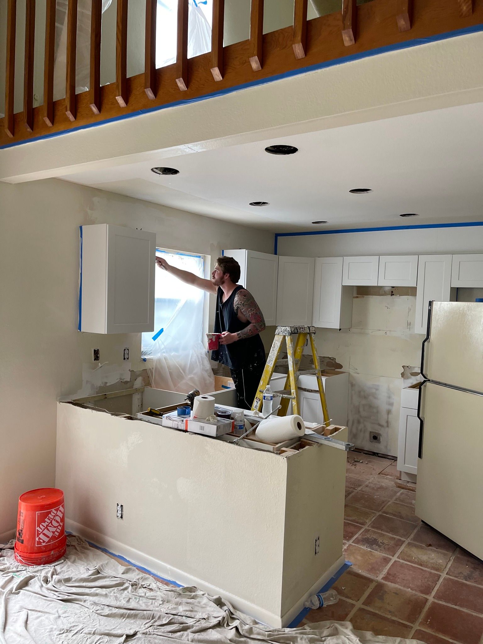 Person painting a white kitchen with an island, ladder, and exposed beams.