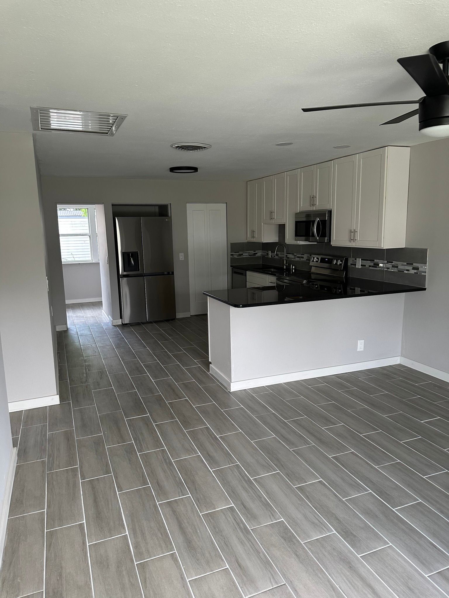 Kitchen with gray wood-look floor, white cabinets, black countertop island, and stainless steel appliances.