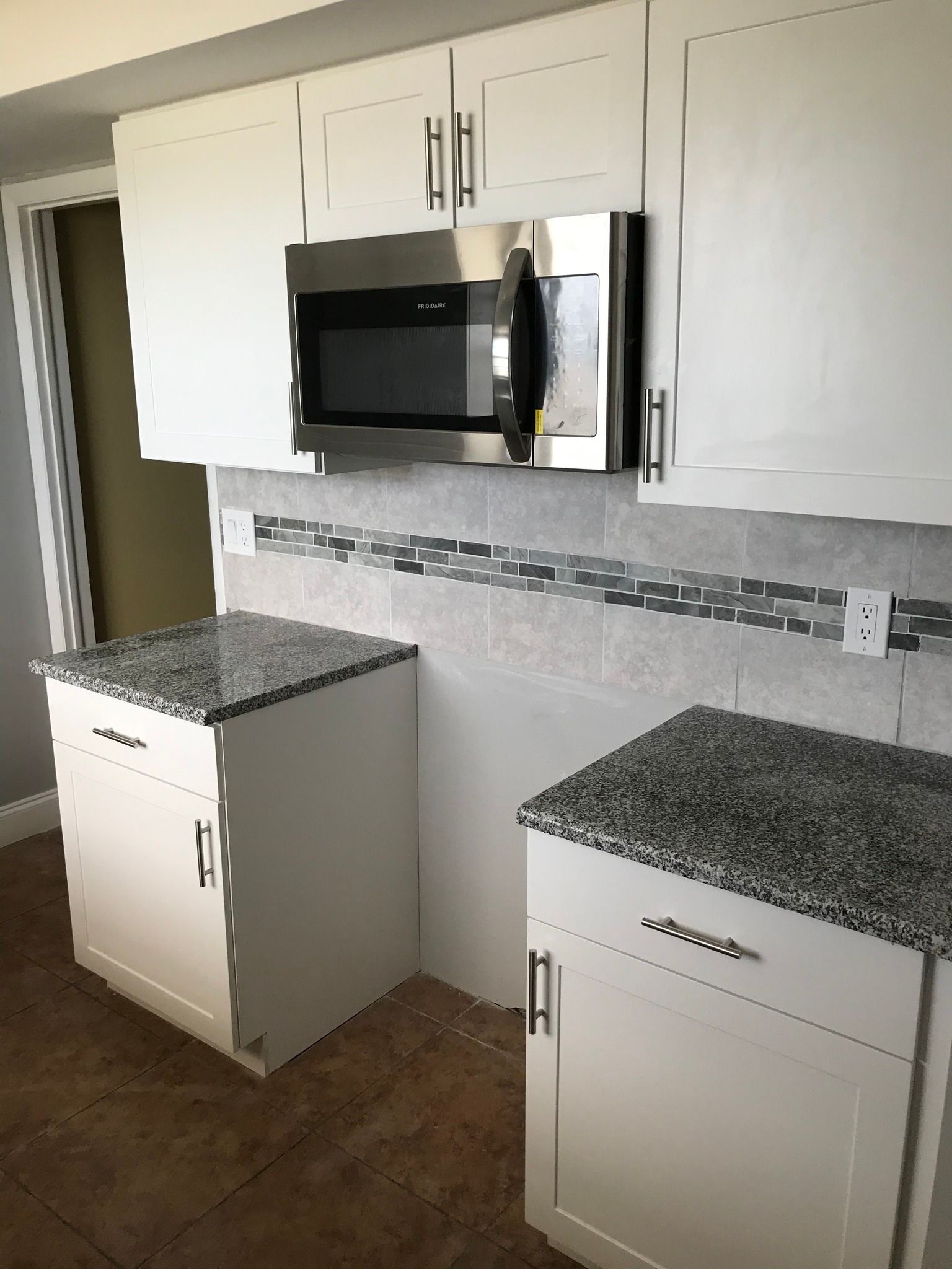 White kitchen cabinets with granite countertops, and stainless steel microwave.
