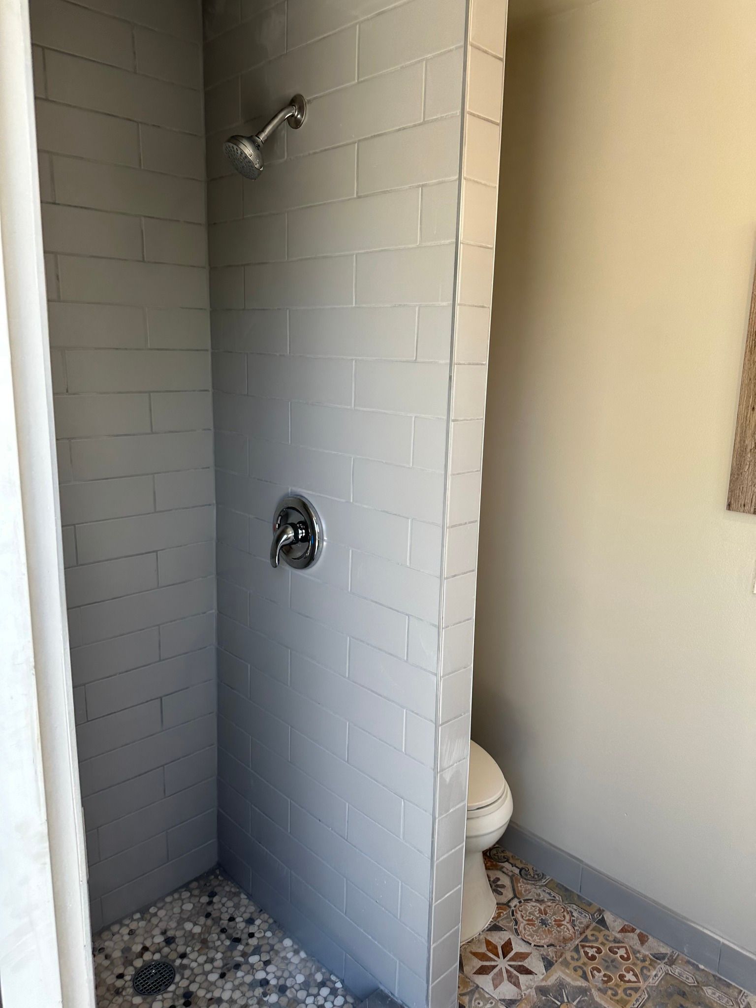 Shower stall with gray tile, toilet, and patterned tile floor.