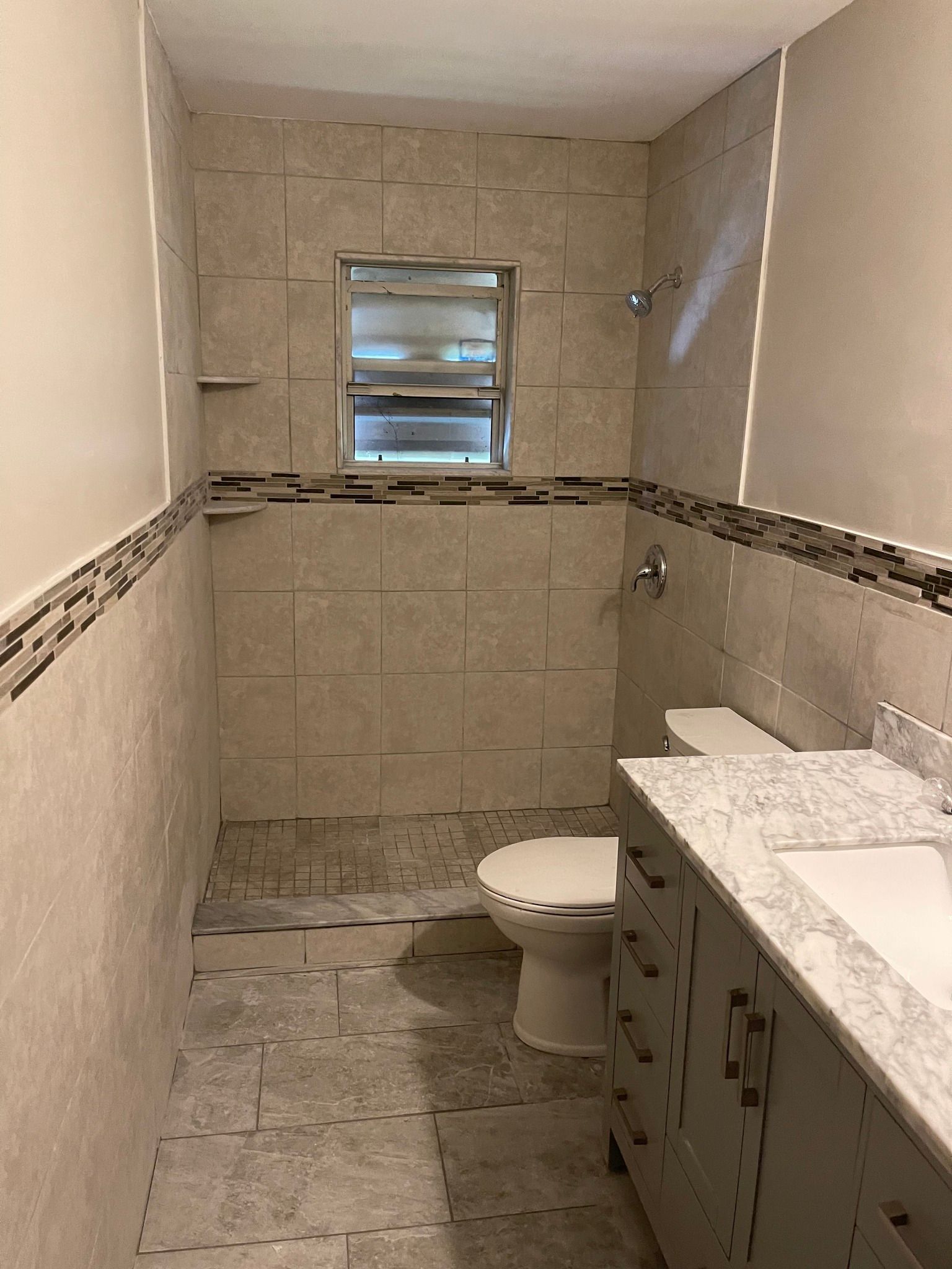 Bathroom under construction with tile walls, a toilet, vanity, and small window.