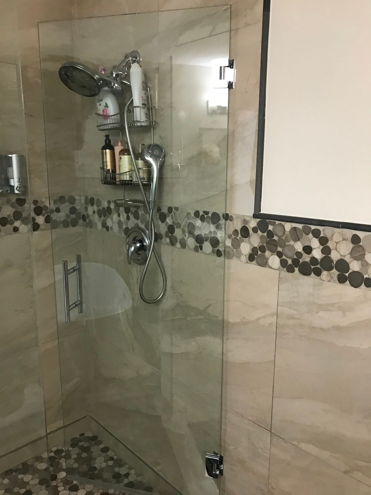Shower stall with glass door, multiple shower heads, and soap/shampoo bottles.