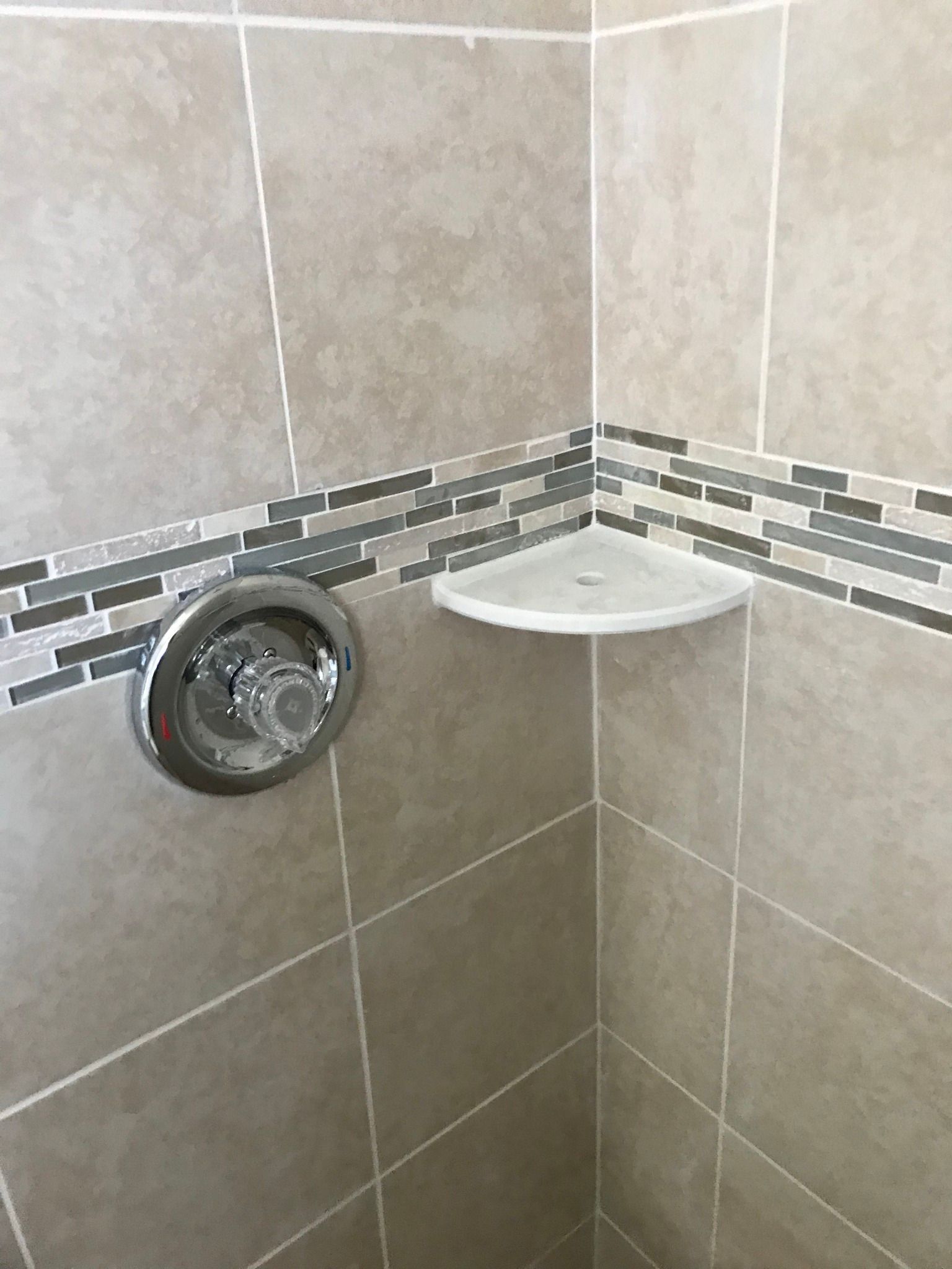 Shower interior with beige tiles, mosaic accent, chrome faucet, and corner shelf.