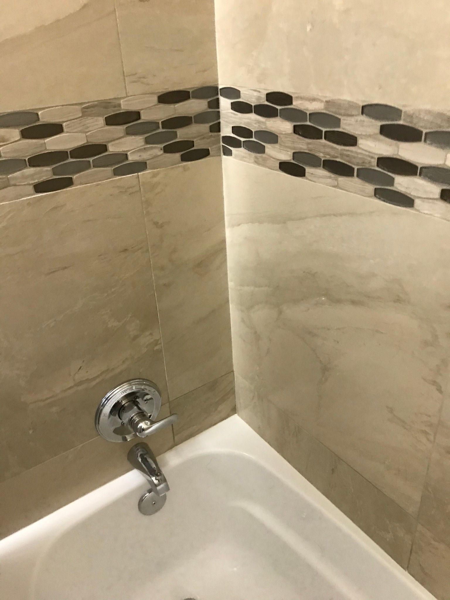 Bathroom corner with a bathtub and chrome faucet, beige tile walls with a decorative mosaic border.