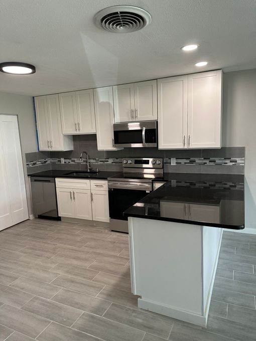 Modern kitchen with white cabinets, stainless steel appliances, gray tile backsplash, and island.