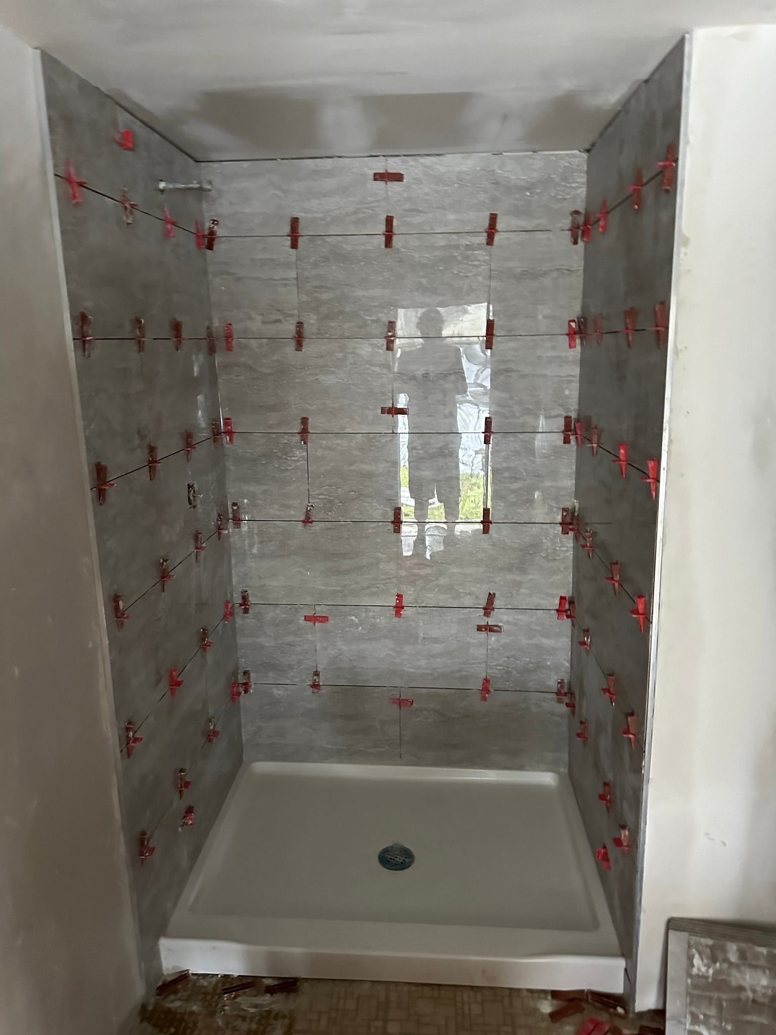 Shower stall with gray tiled walls, red tile spacers, and white base.