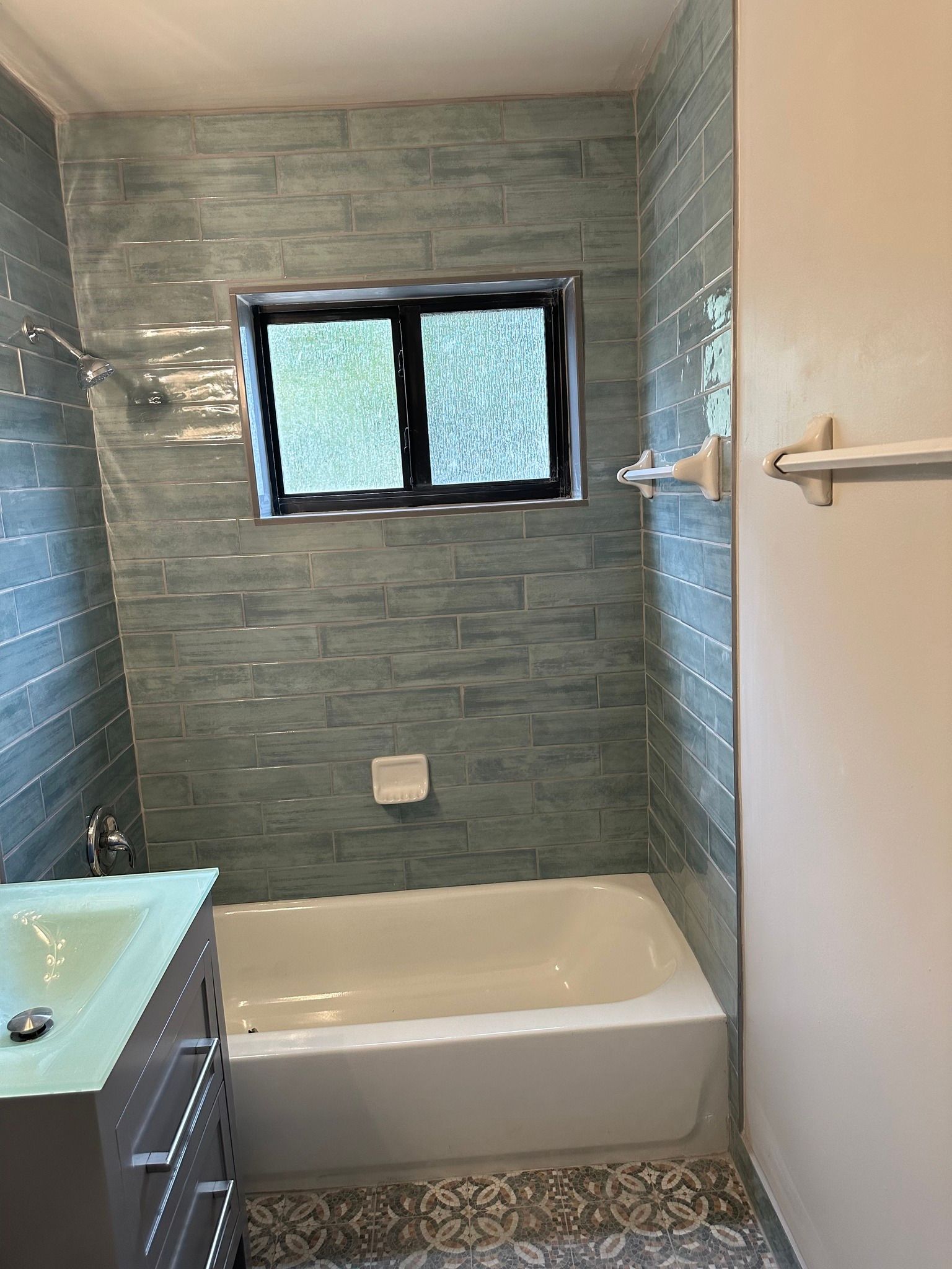 Bathroom with blue-tiled walls, a tub, a vanity, and a small window.