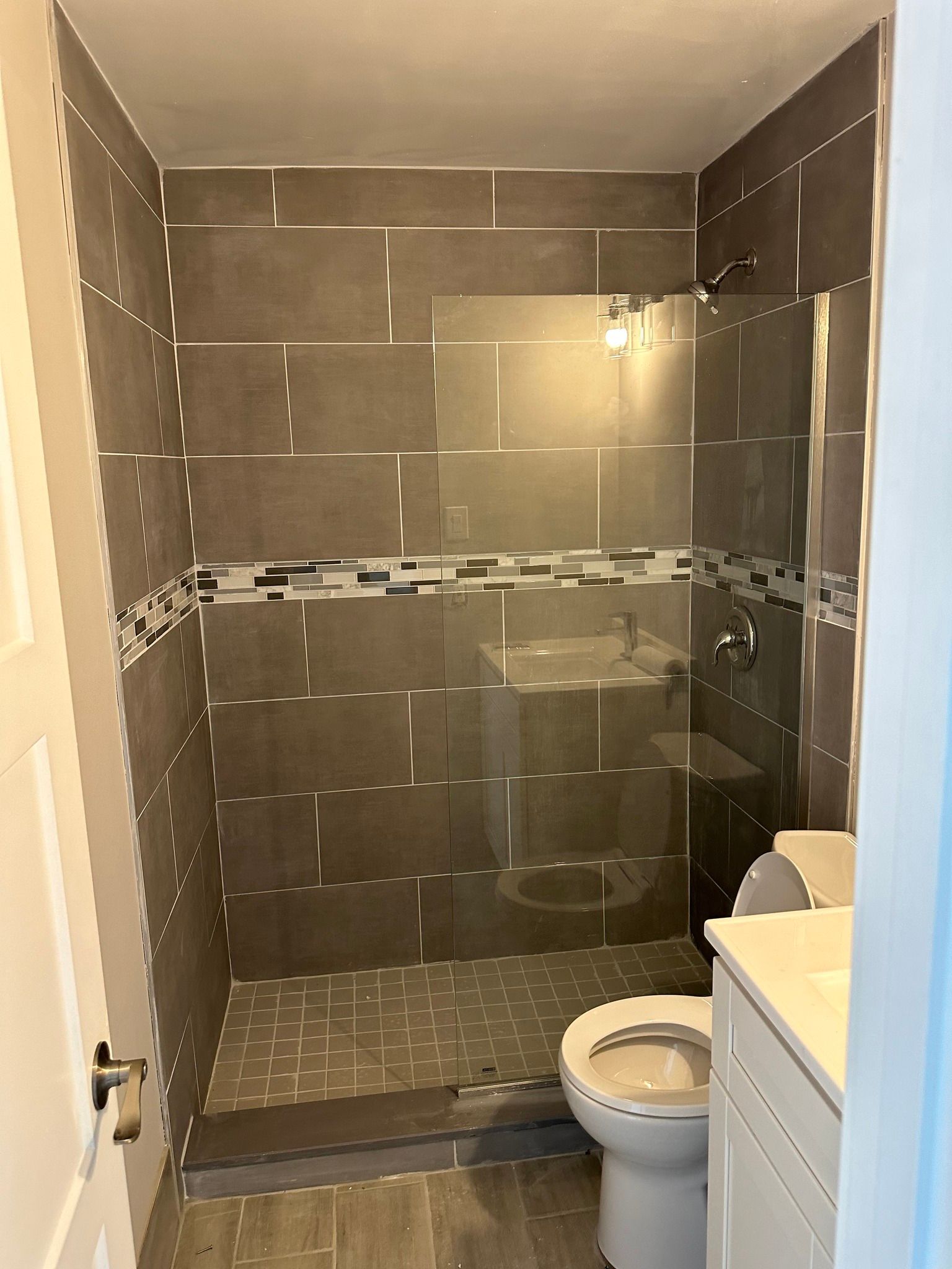 A small, tiled shower with a glass door next to a toilet and vanity.