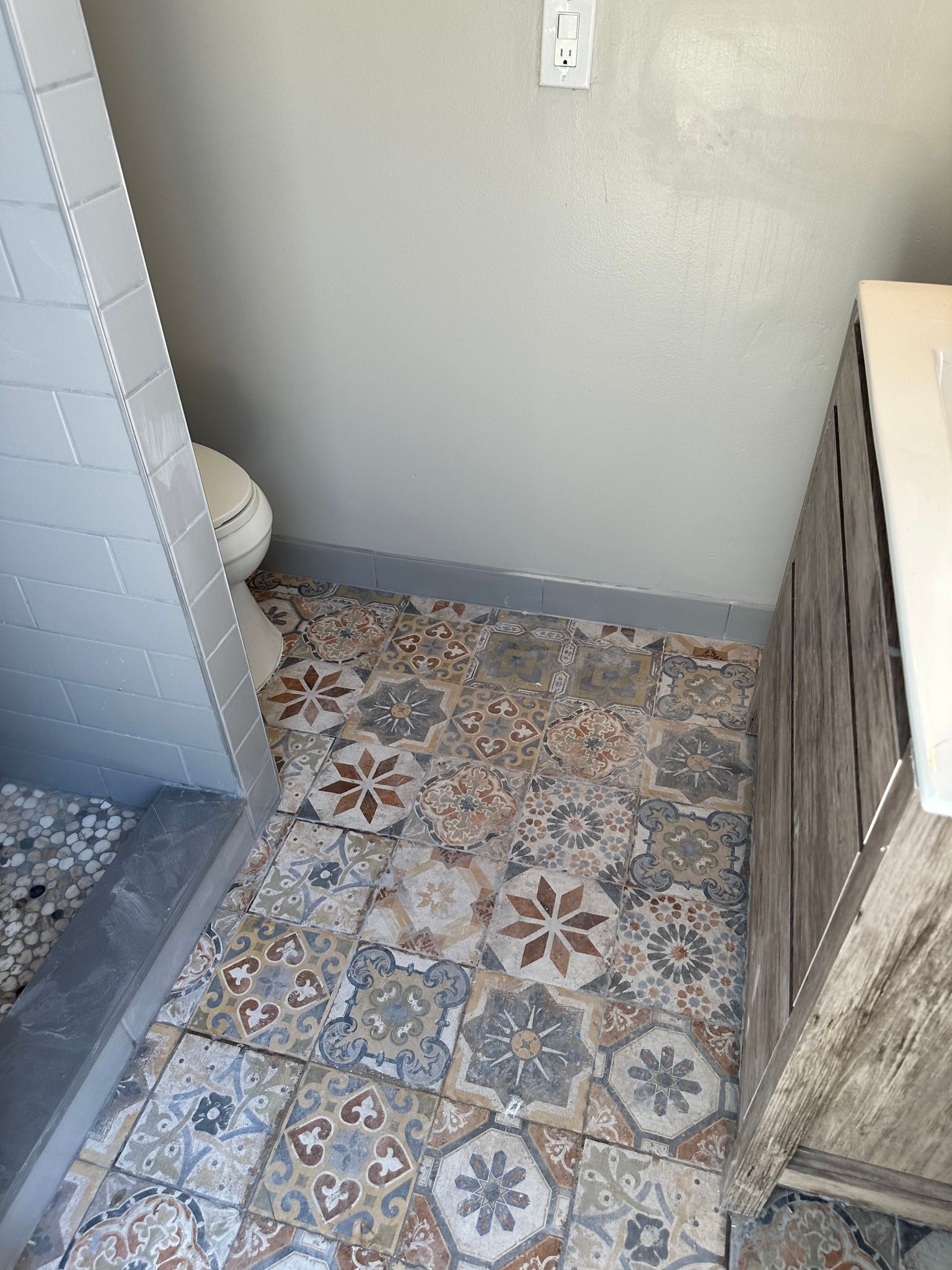 Bathroom with patterned floor tile, gray walls, and a white toilet.