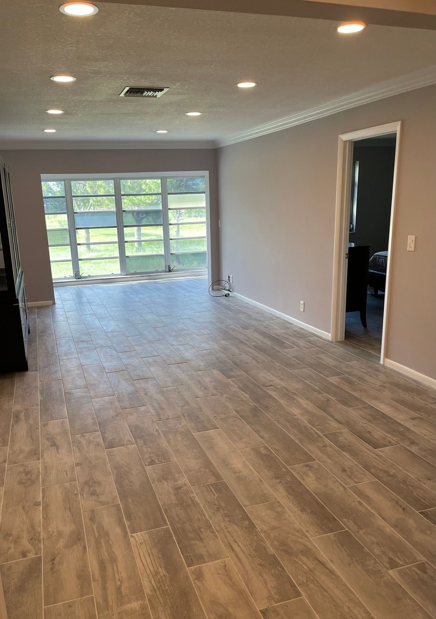 Spacious room with wood-look flooring, large window, and recessed lighting. Light gray walls, white trim, and an open doorway.