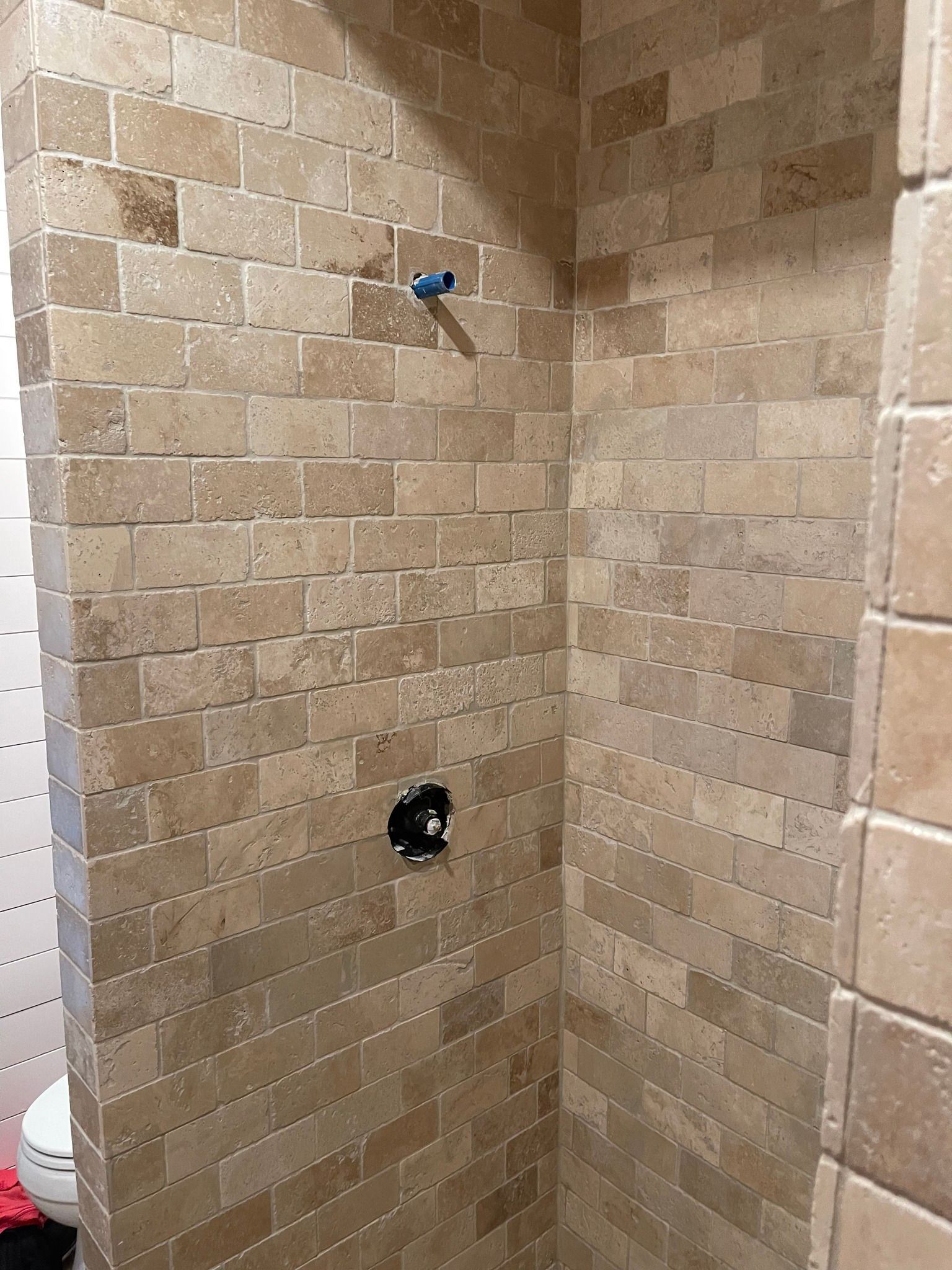 Shower stall with beige brick-style tiled walls. Plumbing fixtures visible, ready for shower head and controls.
