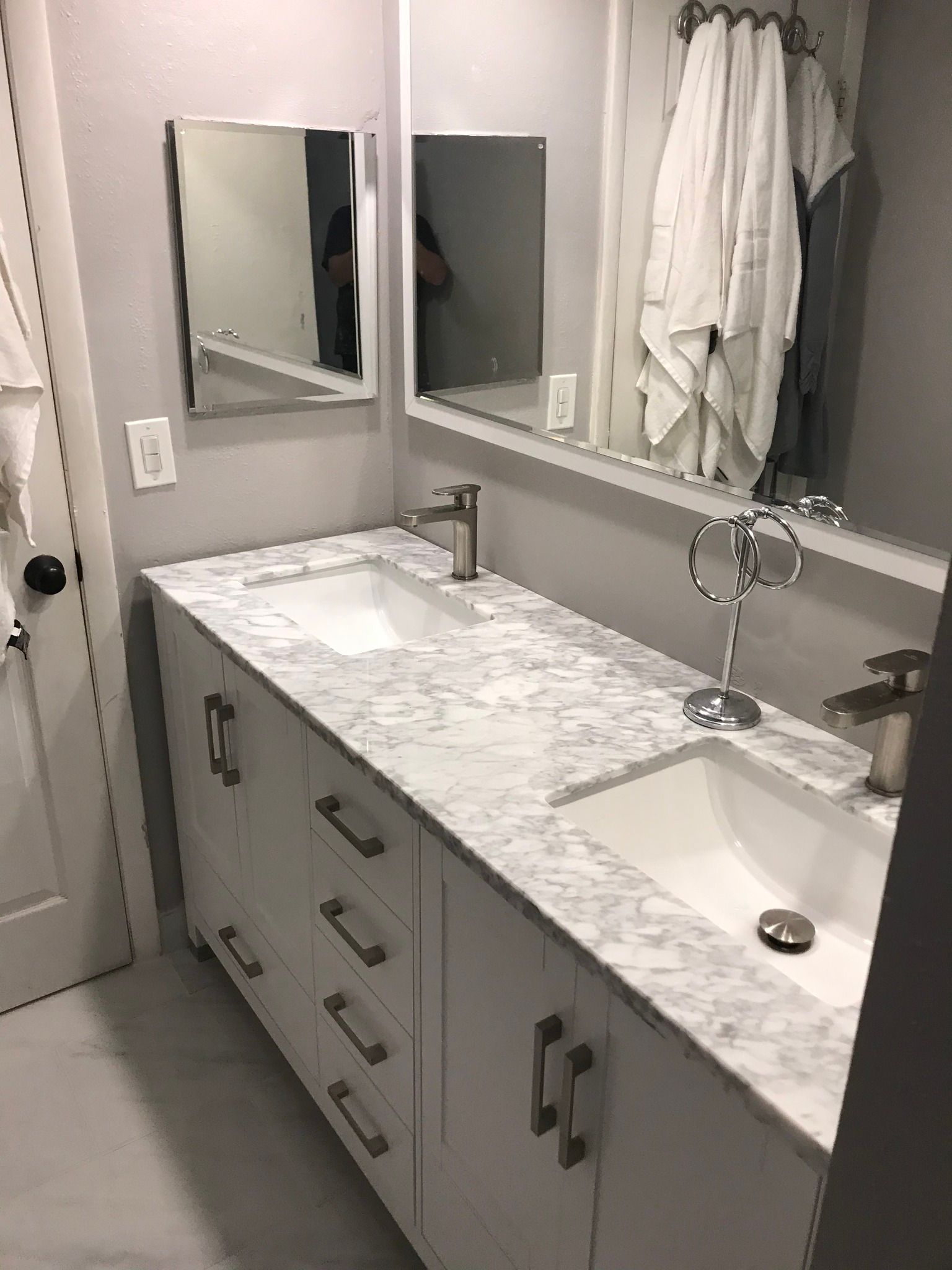 White bathroom vanity with marble countertop, two sinks, mirrors, and a towel rack.