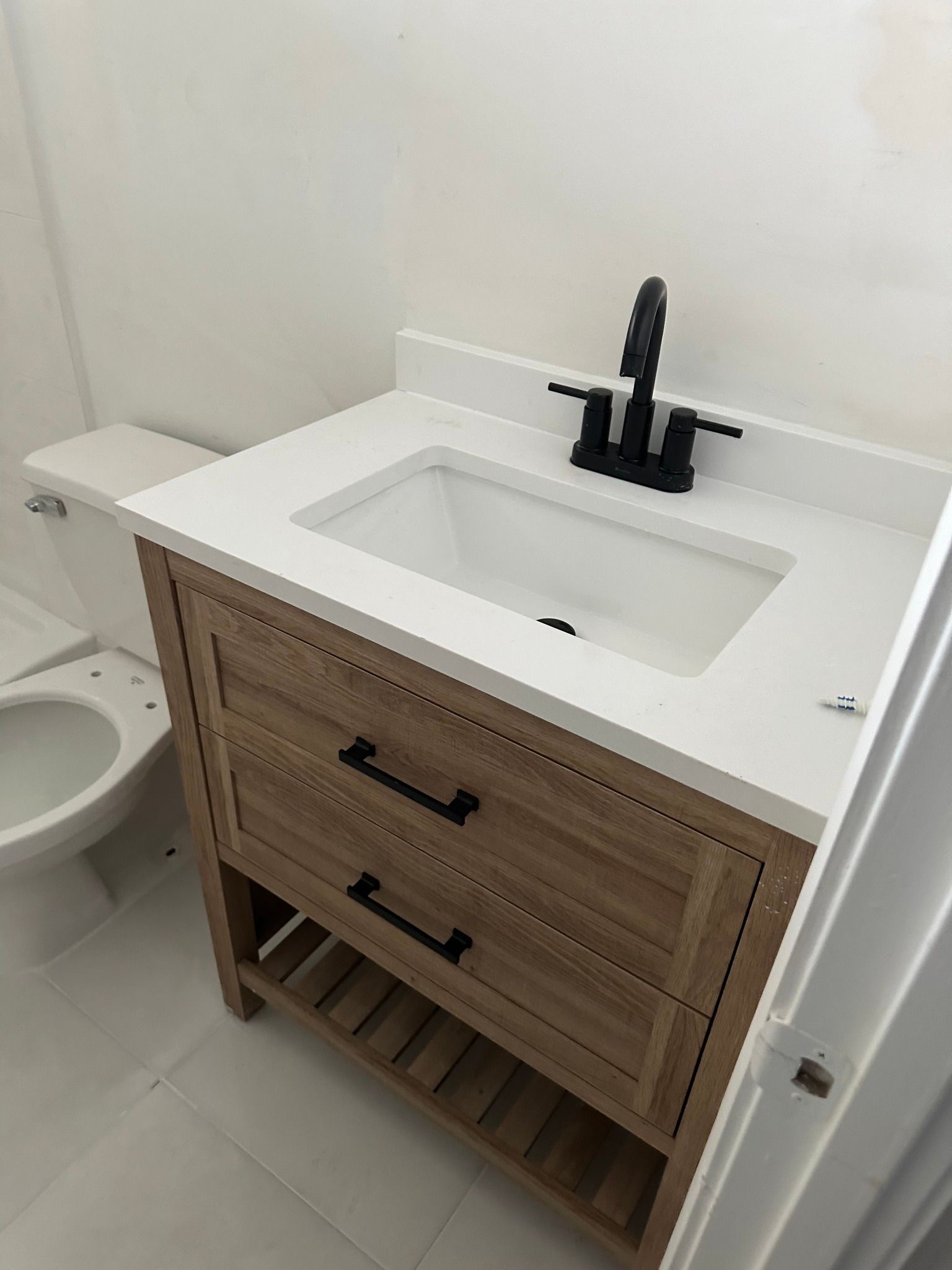 Bathroom vanity with a light wood finish, white countertop and sink, black faucet and pulls.
