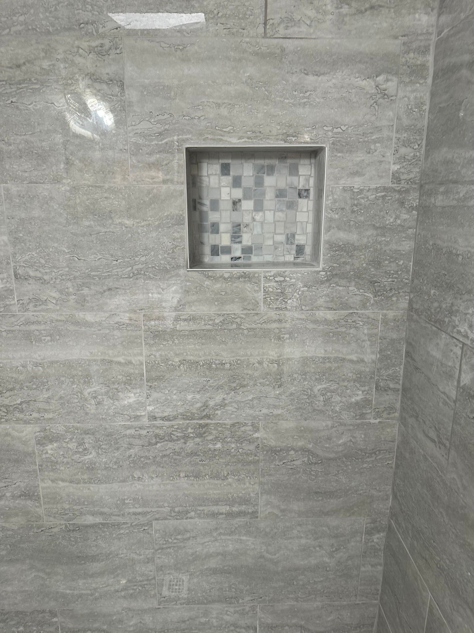 Shower wall with recessed shelf, gray tile, mosaic tile in shelf.
