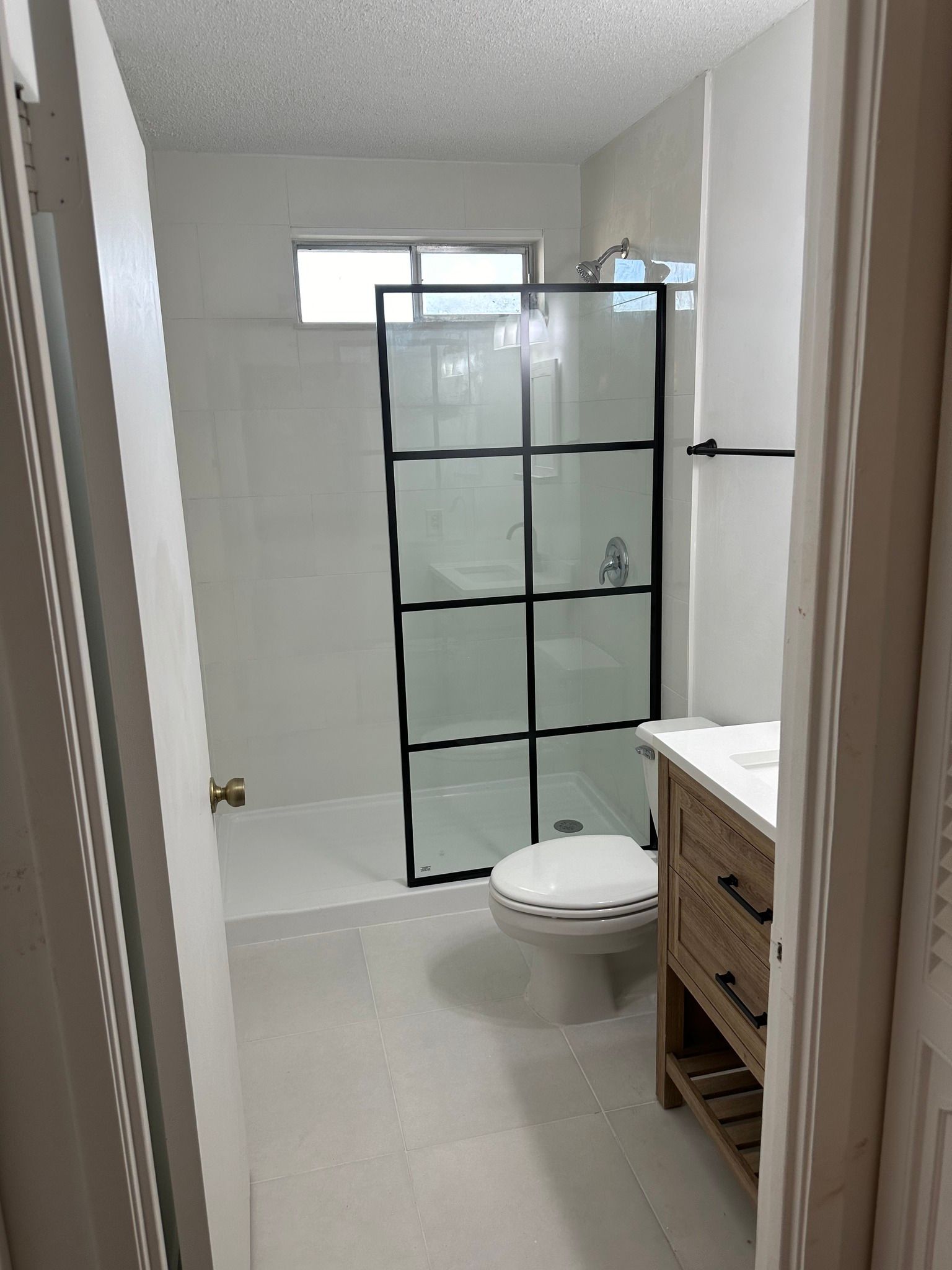 Bathroom with white tile, black-framed shower, toilet, vanity, and partially open door.
