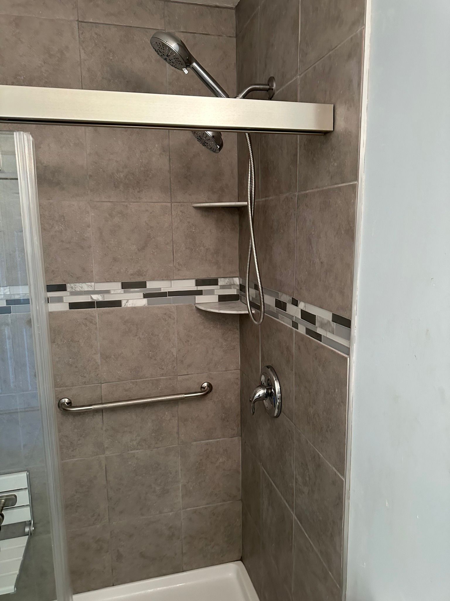 Shower with gray tile, silver fixtures, and a grab bar, designed for accessibility.