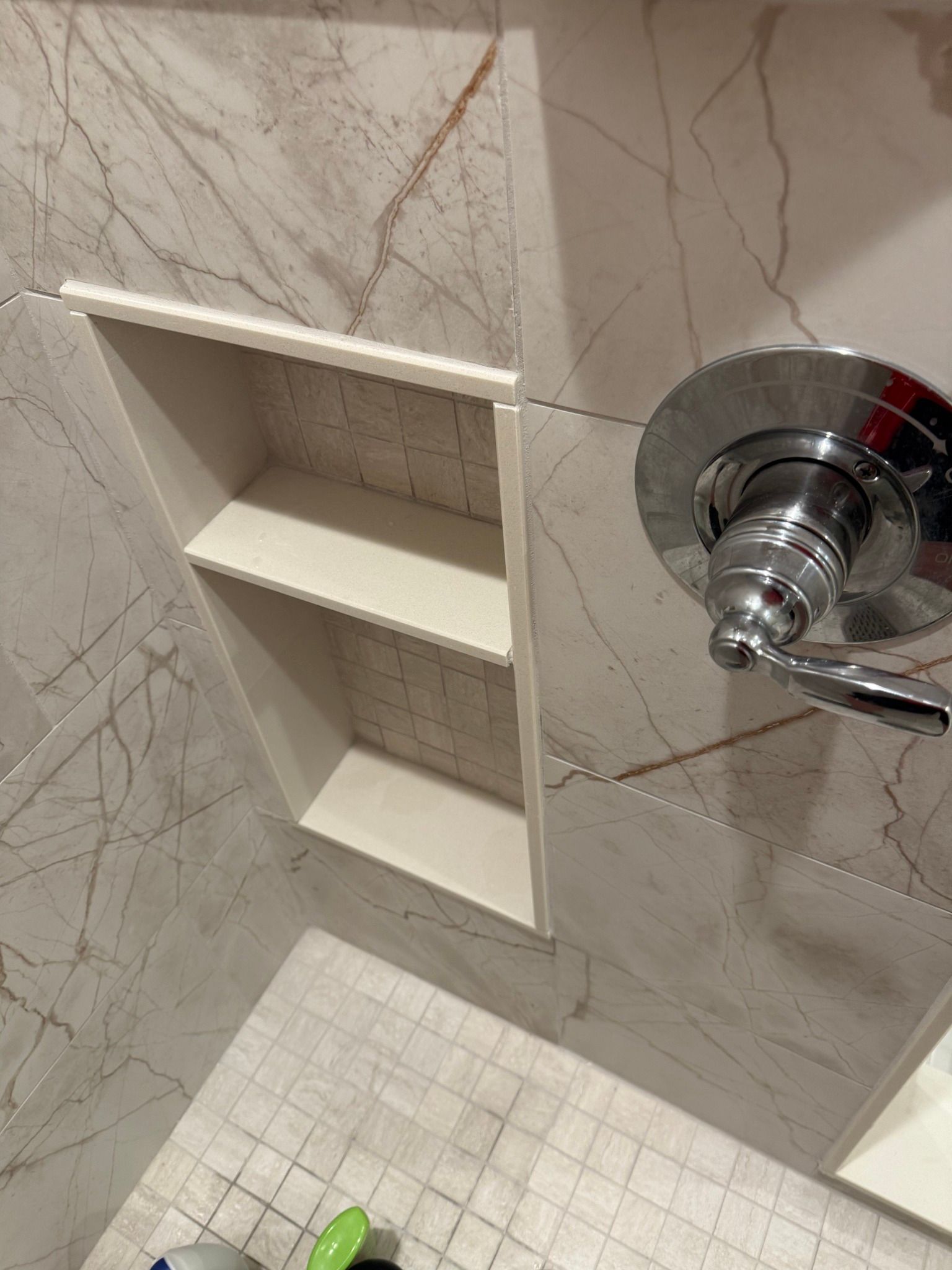 Shower niche with two shelves built into a tiled wall. Chrome faucet on the right.