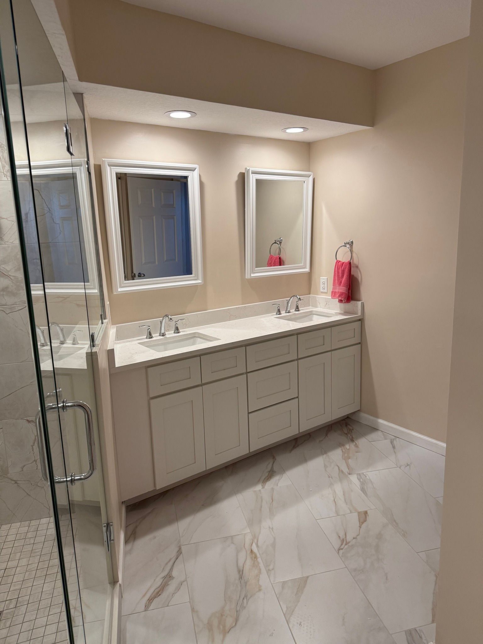 Bathroom with double vanity, marble floors, and glass shower.