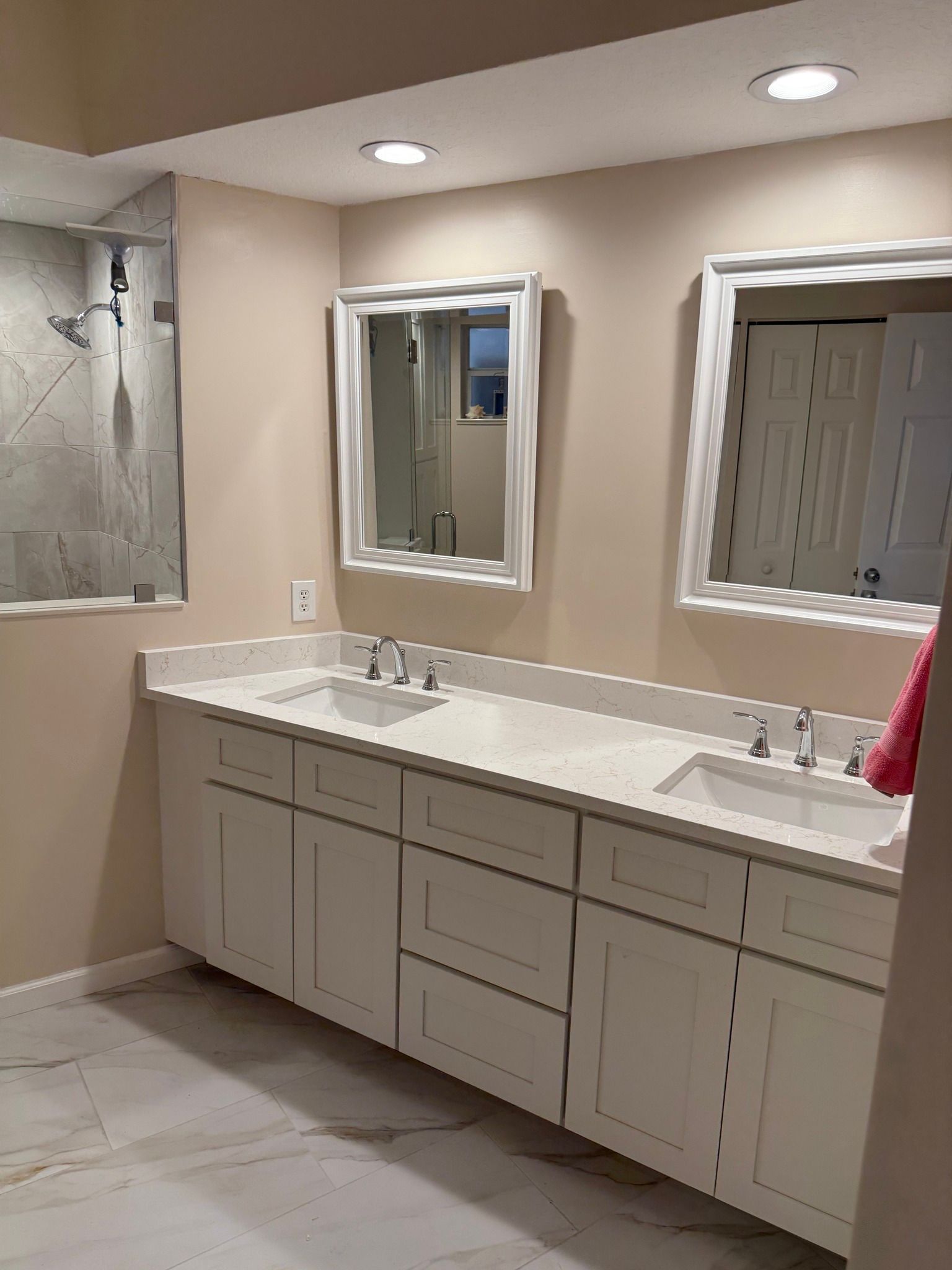 Bathroom with white double vanity, mirrors, and a shower, in a room with light-colored walls and tile floor.