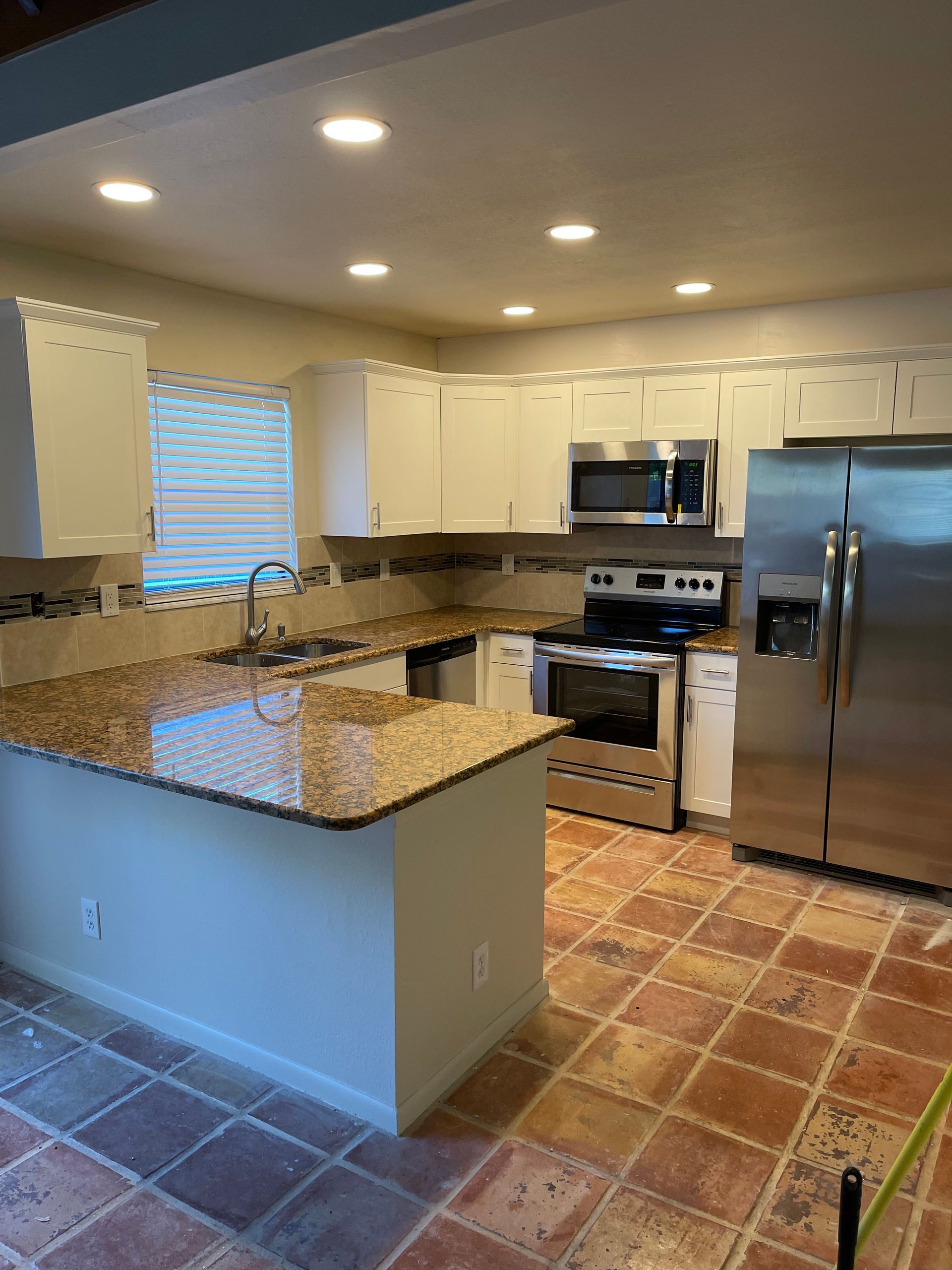 Kitchen with white cabinets, granite countertops, stainless steel appliances, and terracotta tile flooring.