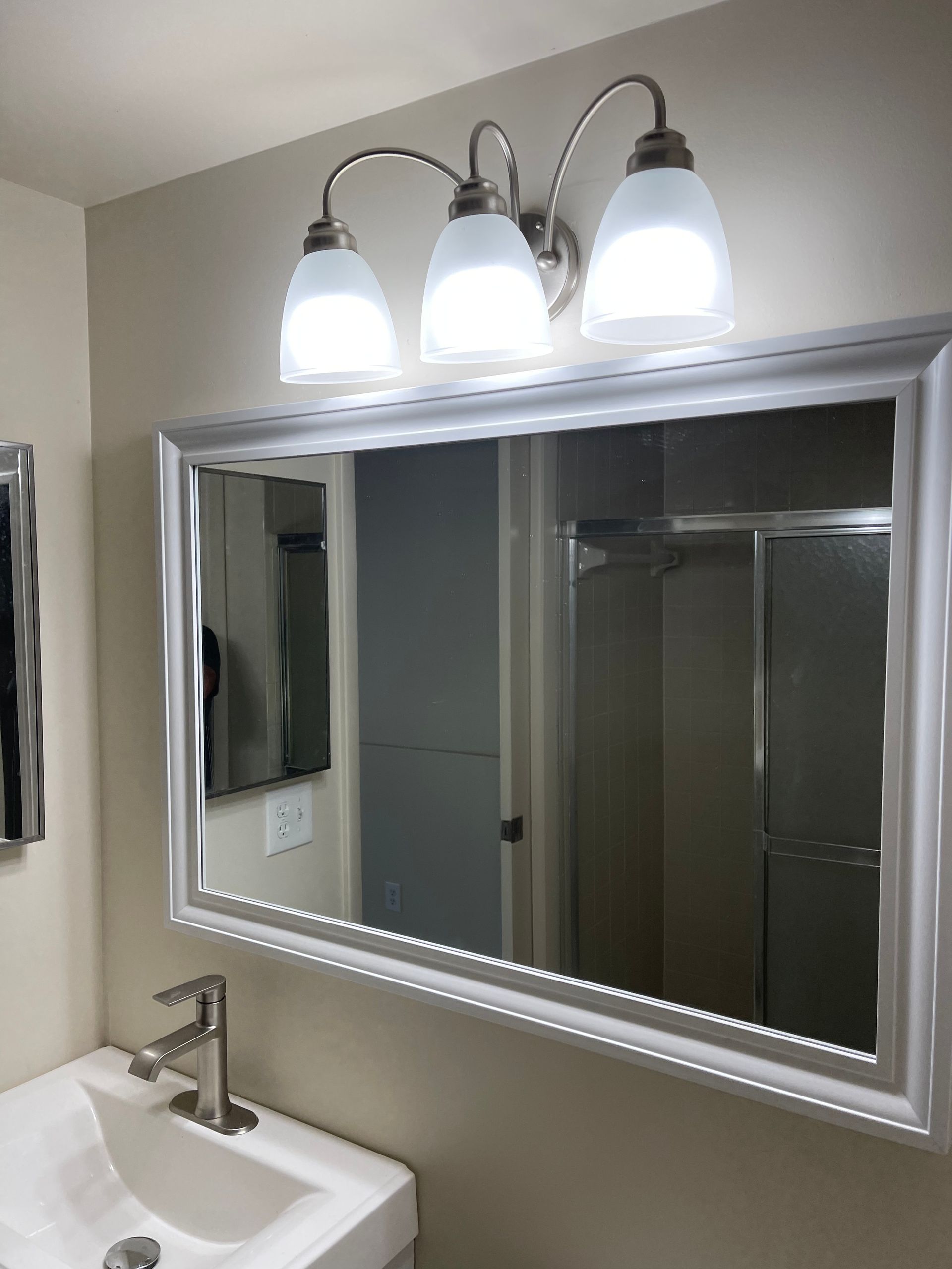 Bathroom with a white sink, large mirror, and three-light fixture above it.
