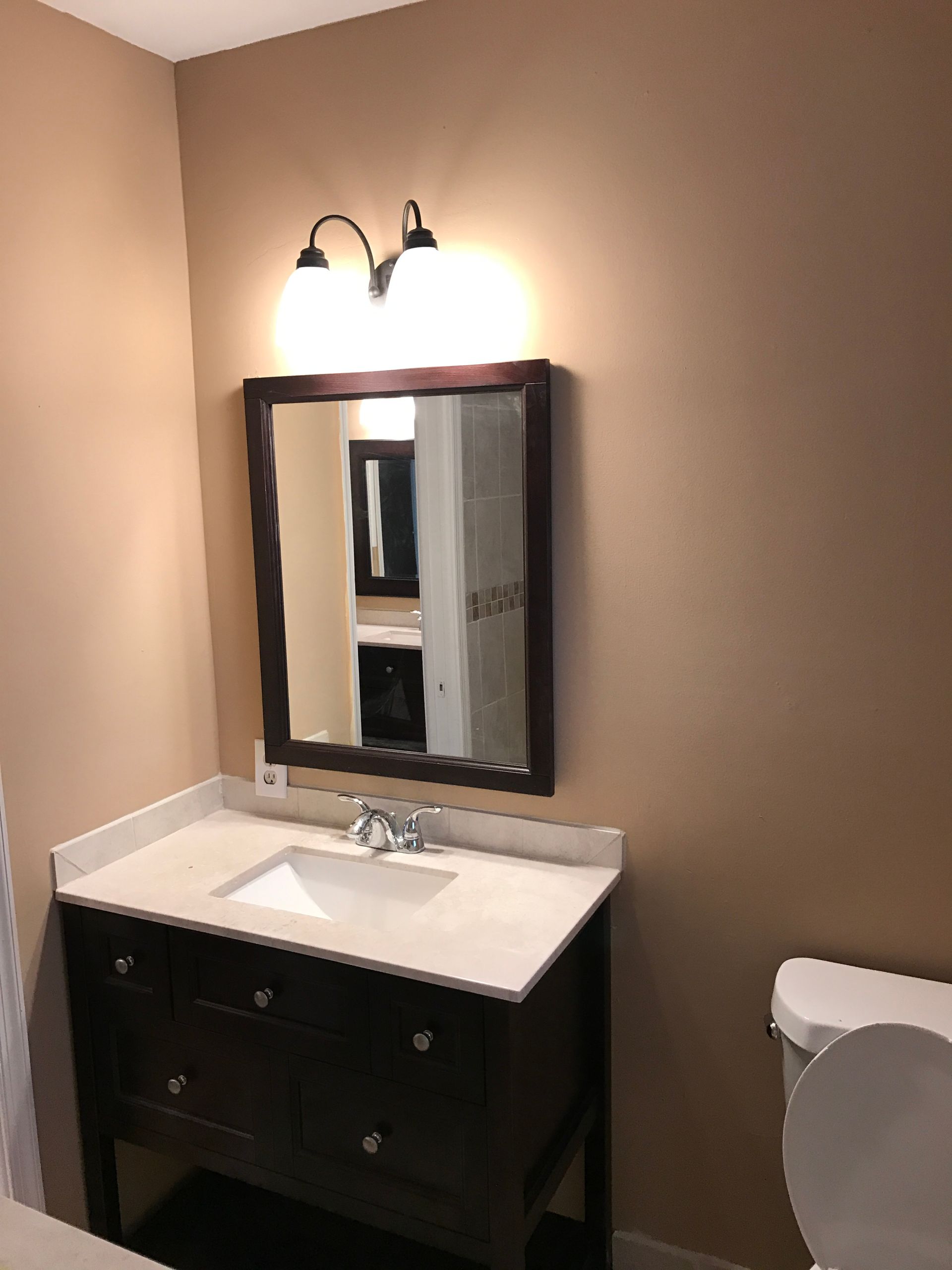 Bathroom with dark brown vanity, white countertop, mirror, and toilet.