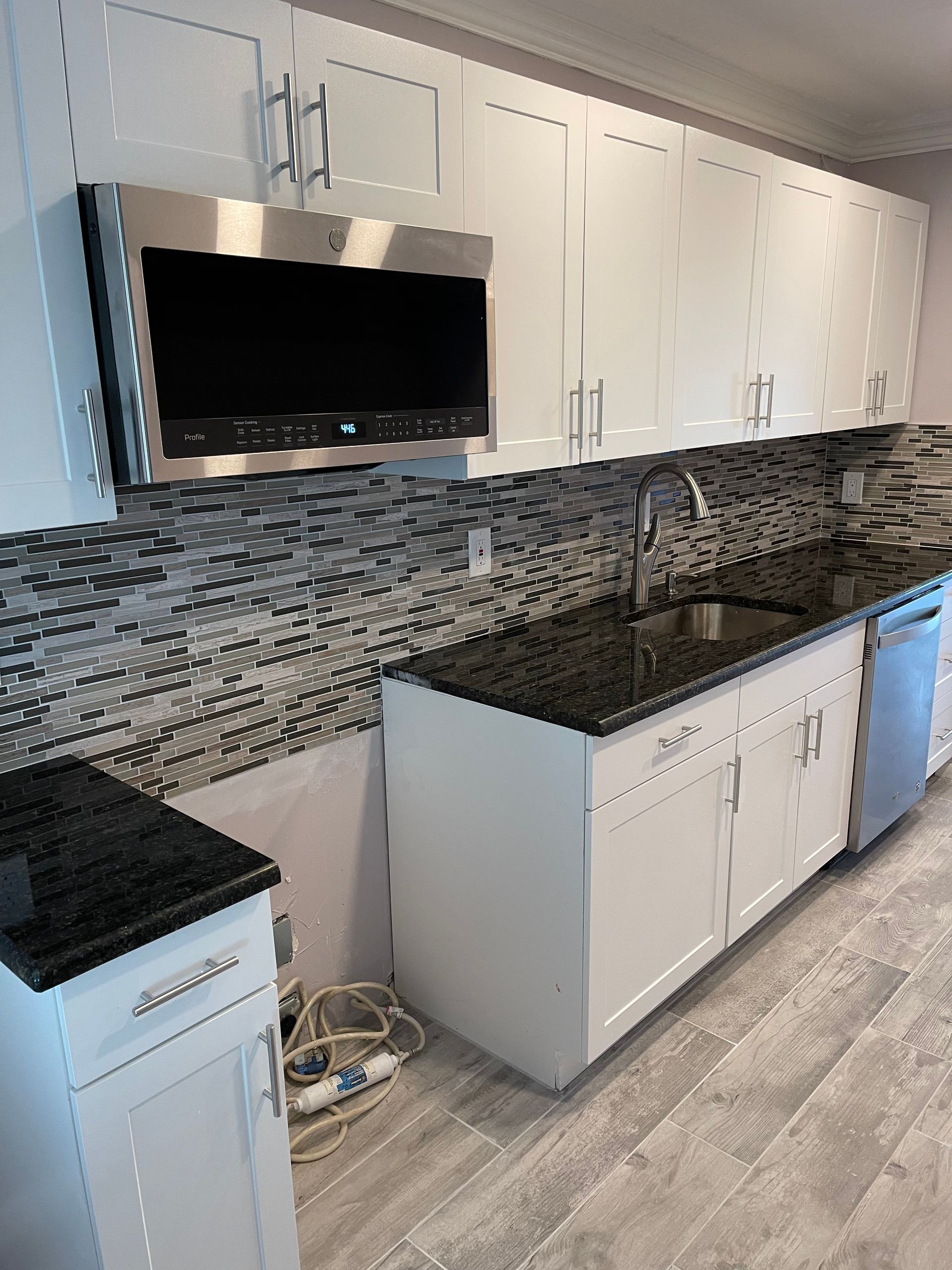 White kitchen cabinets with a microwave, black countertop, and mosaic backsplash.