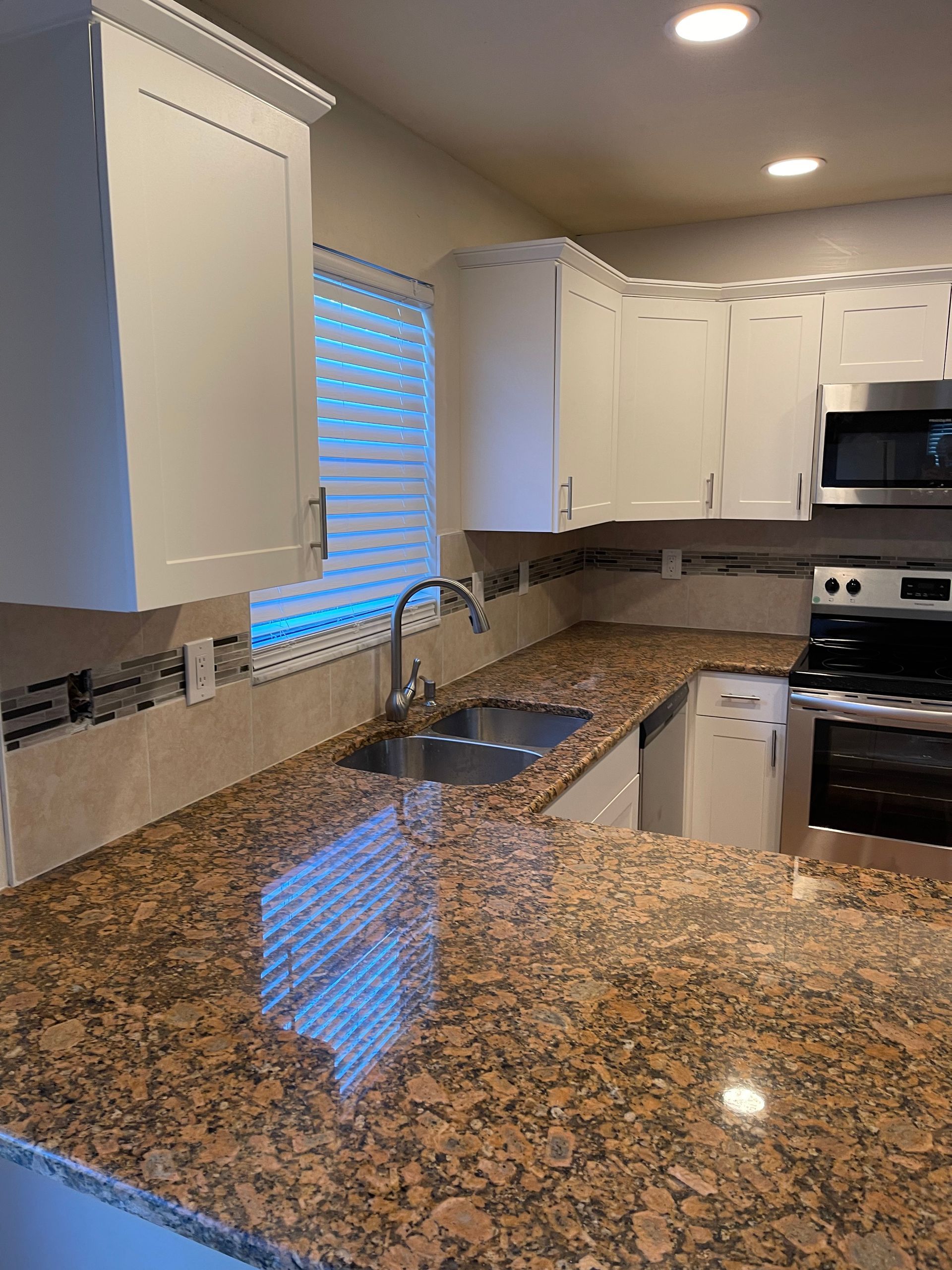 Kitchen with white cabinets, brown granite countertops, stainless steel appliances, and a window.
