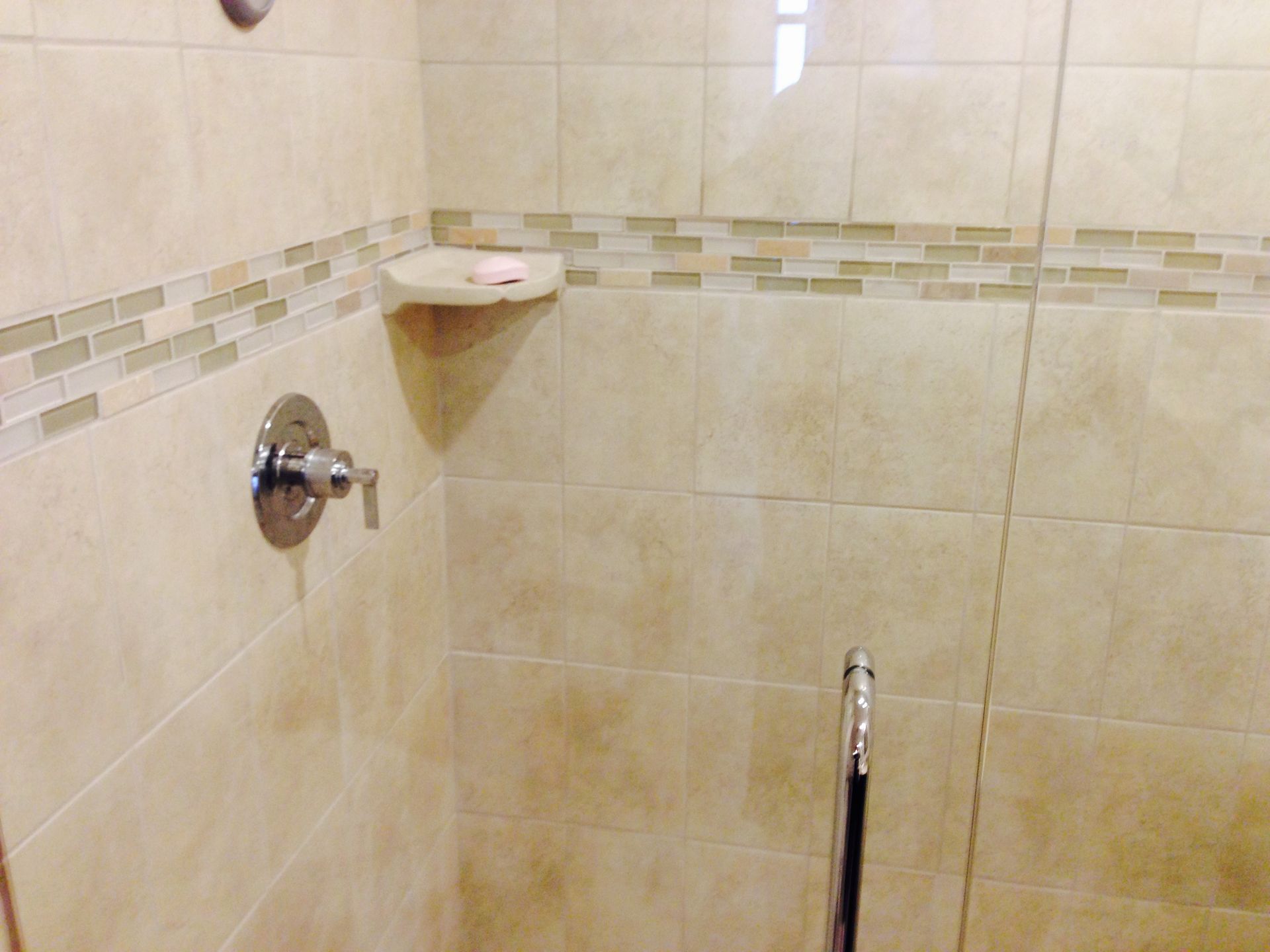 Shower stall with beige tiles, a decorative accent, and a soap dish.