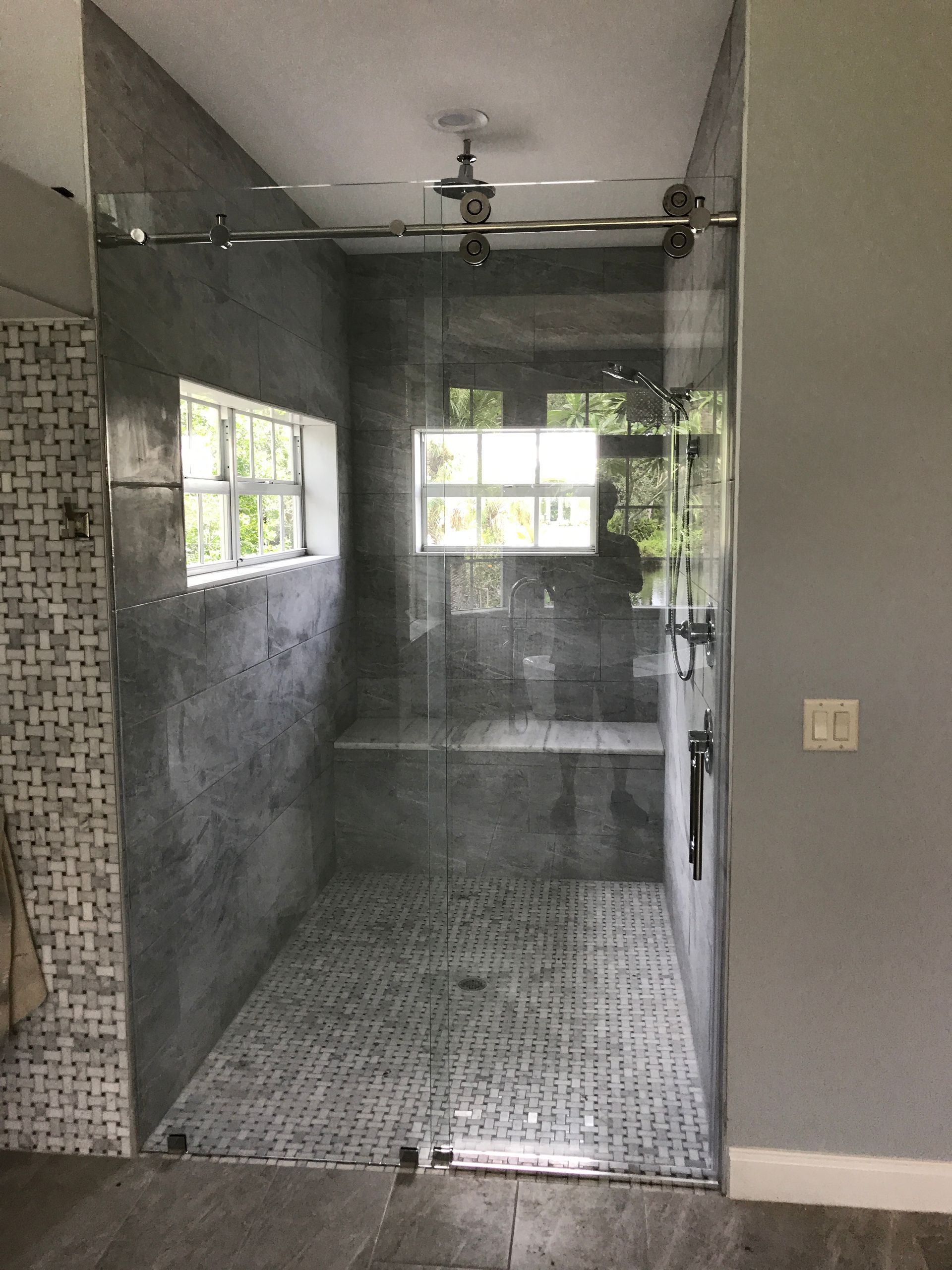 Gray tiled shower with glass door, window, and bench.