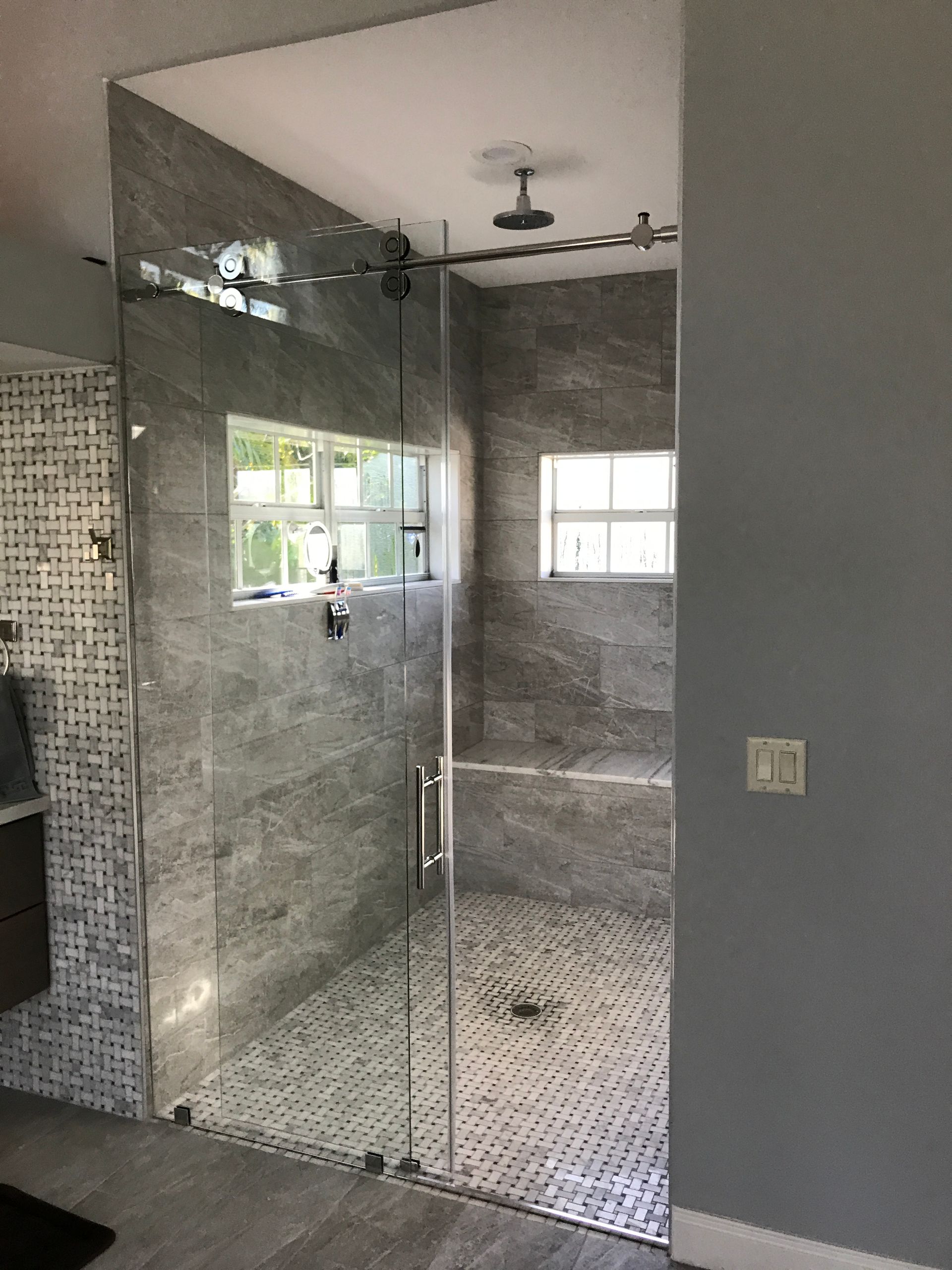 Modern glass shower enclosure with gray tile walls and a small window.