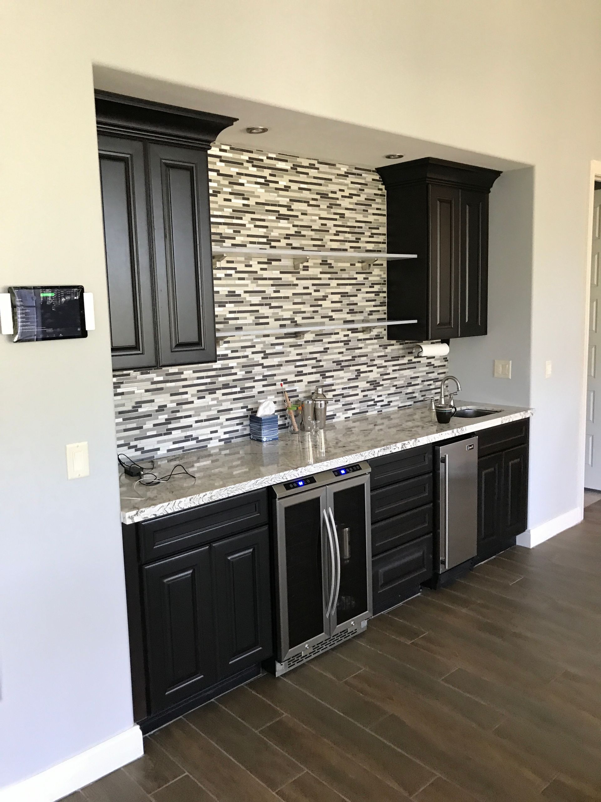 A wet bar area with black cabinets, a mosaic backsplash, and a wine cooler.