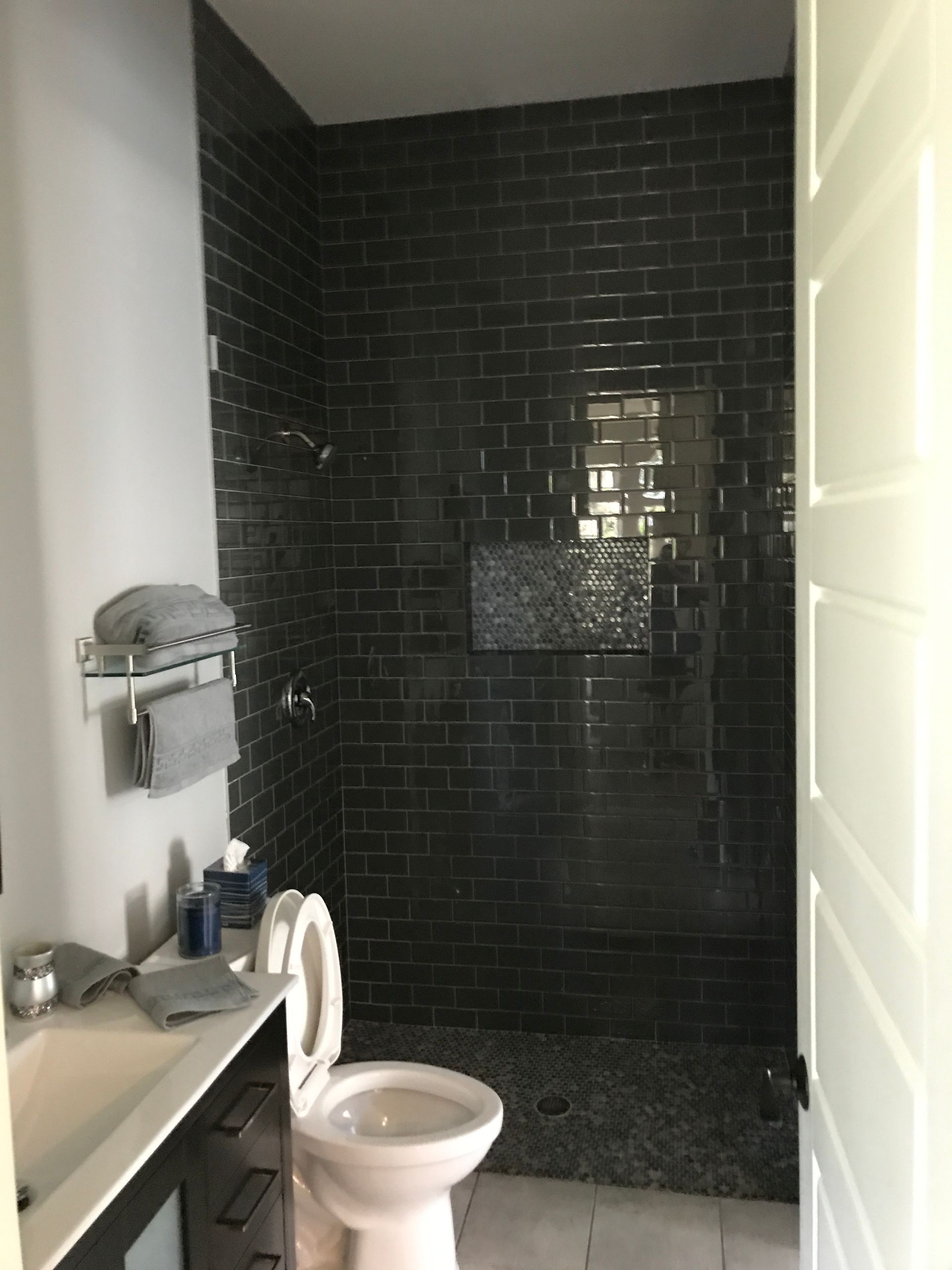 Bathroom with dark tiled shower, toilet, sink, and towel rack.