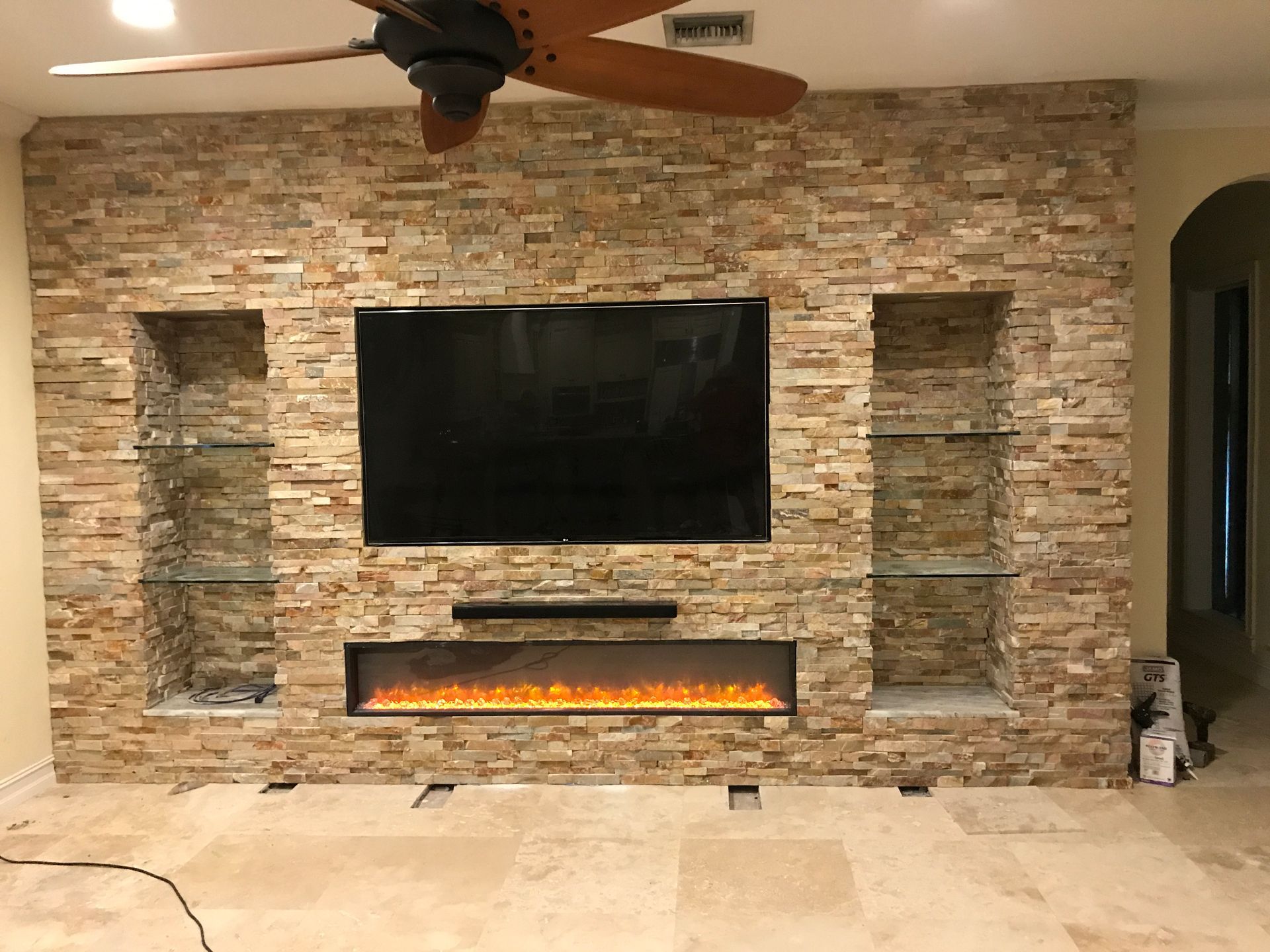 Stone wall with a mounted TV, fireplace, and built-in shelves.